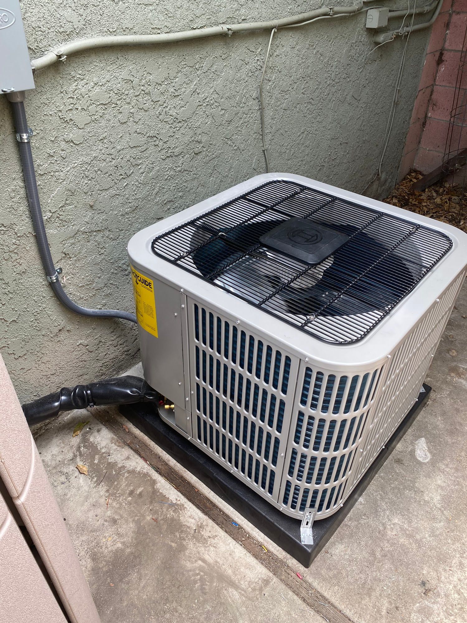 Air conditioning unit next to a wall, with black electrical conduit and a black platform.