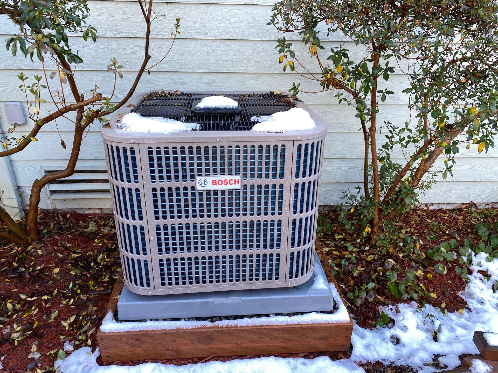 AC unit covered with snow in a yard. Bosch logo visible.