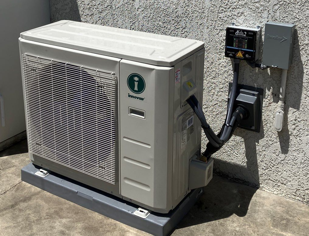 Outdoor air conditioning unit with electrical components attached to a stucco wall.