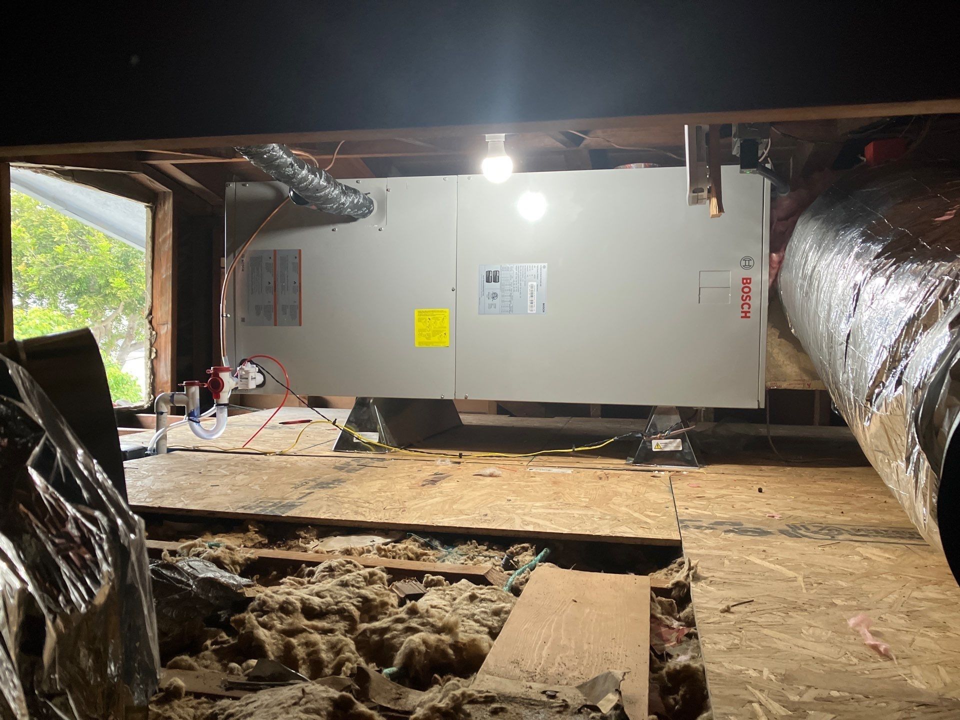 HVAC unit installed in a crawlspace; ducts and insulation visible, illuminated by a light.