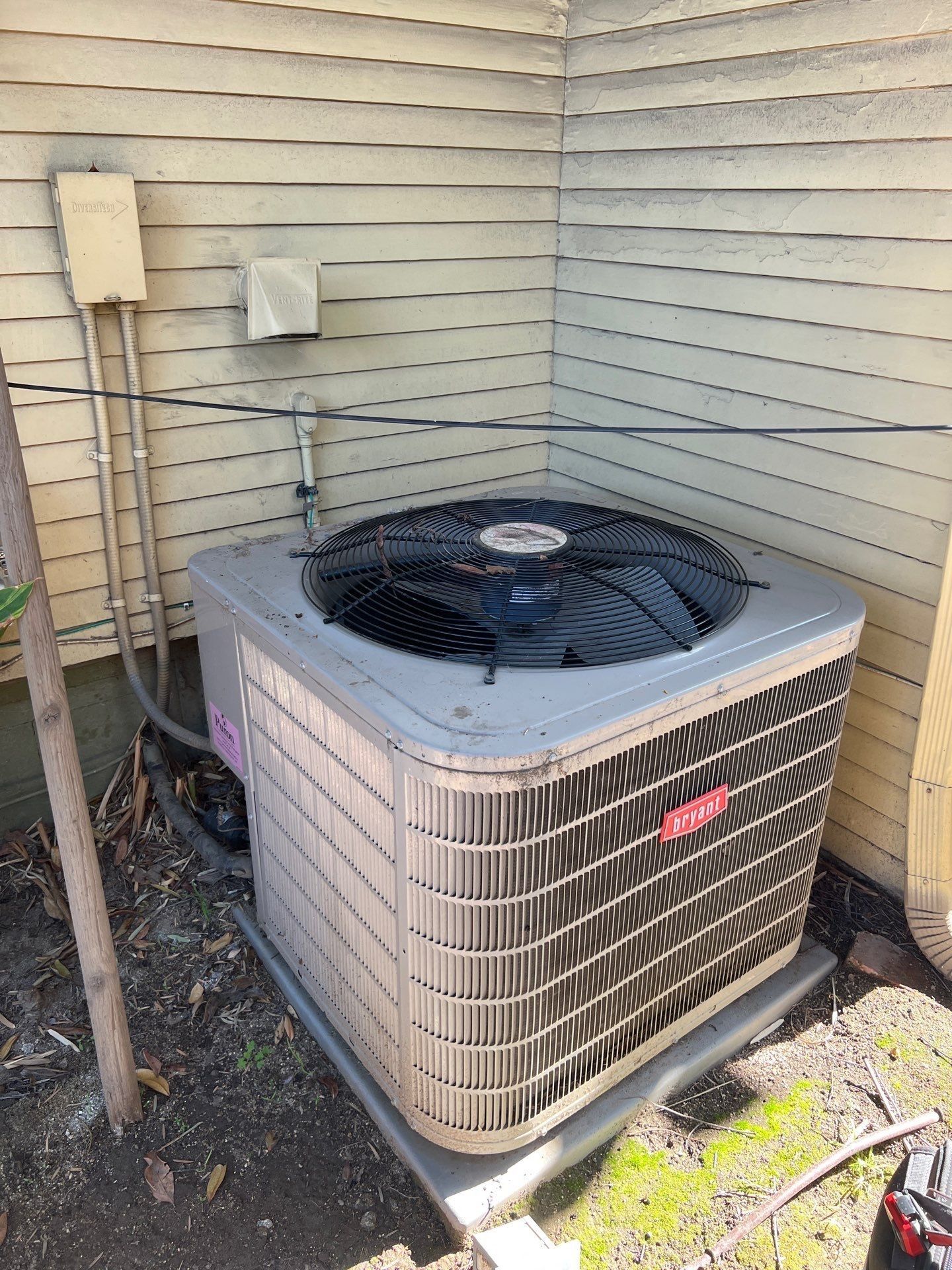 Air conditioner unit outside house, gray, with fan on top and siding background.