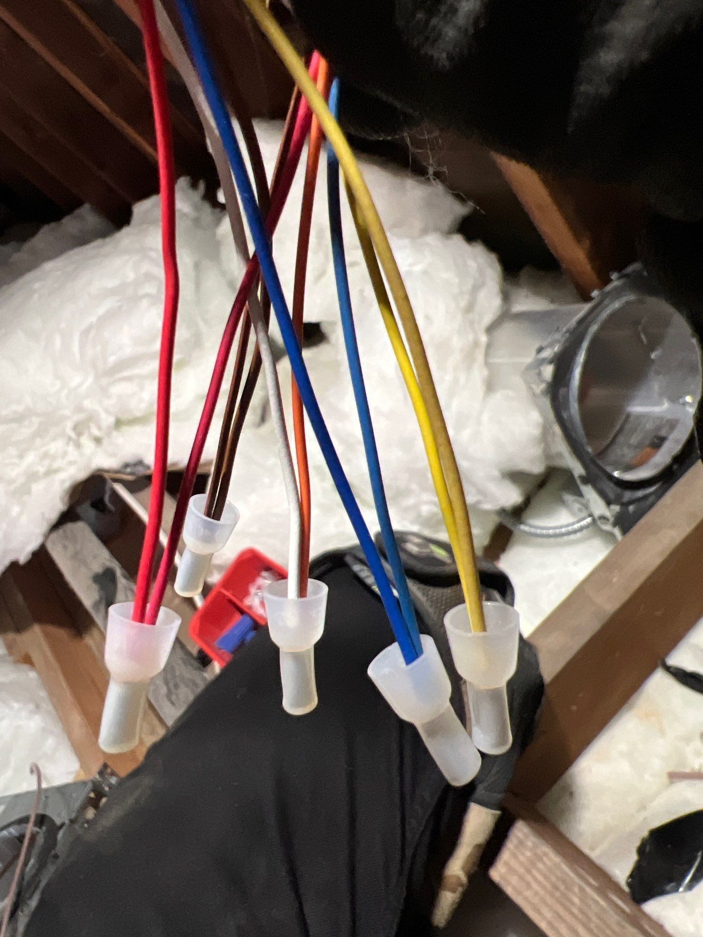 Electrical wires with crimped connectors, various colors, in an attic setting.