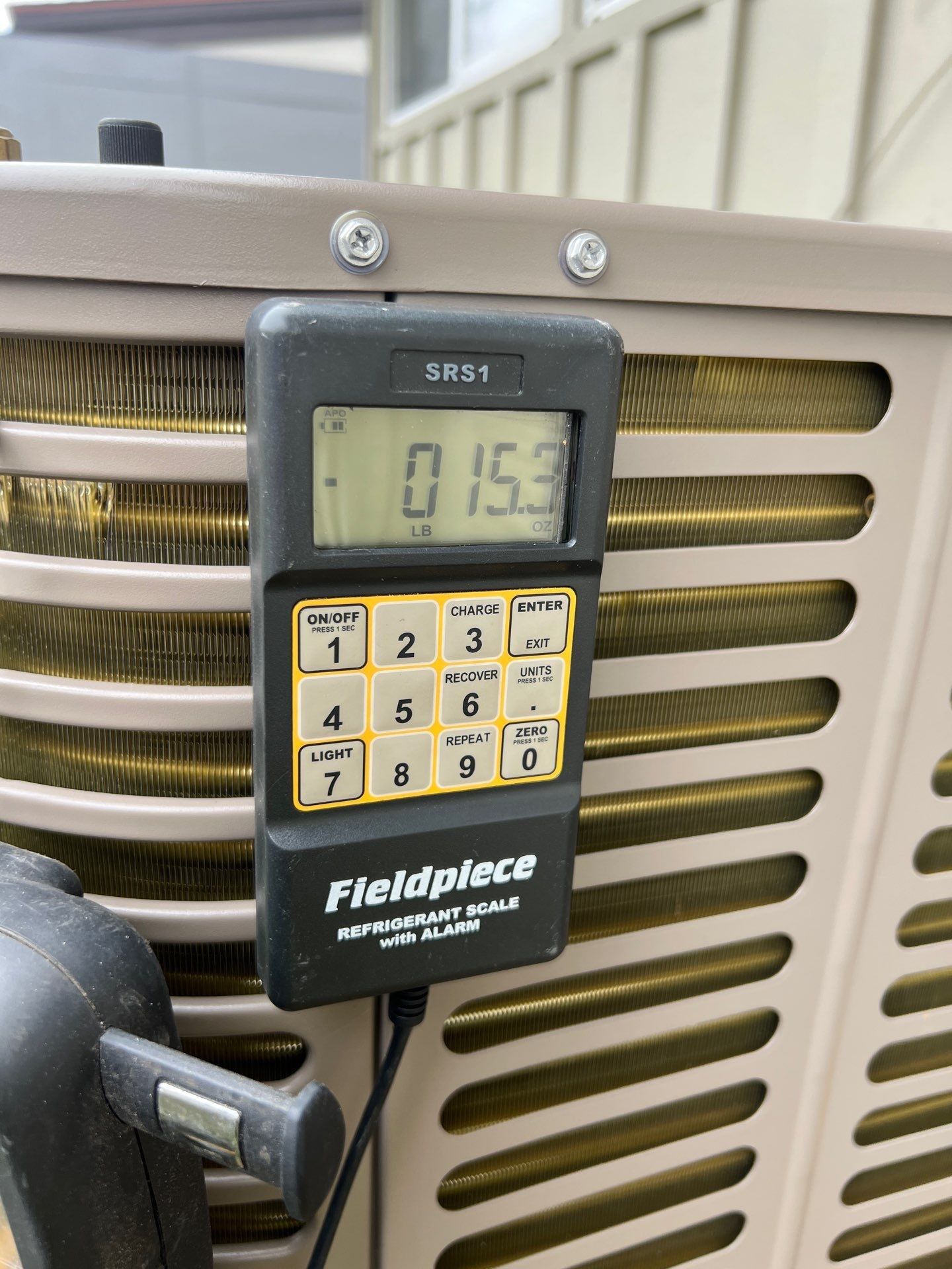 Fieldpiece digital scale on an AC unit displays 153.3, measuring refrigerant charge.