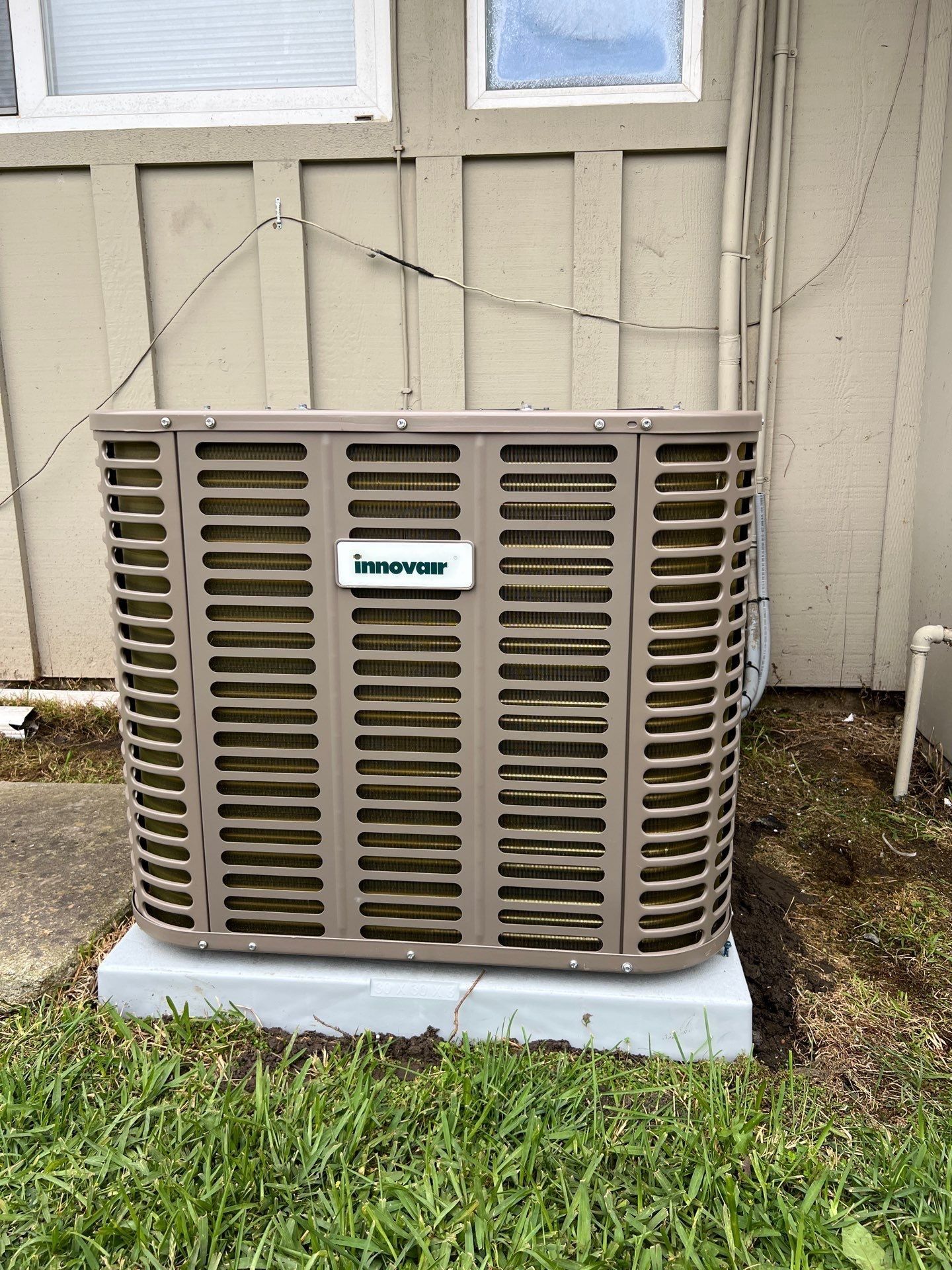 Tan Inovev air conditioning unit on a concrete base next to a building with beige siding.