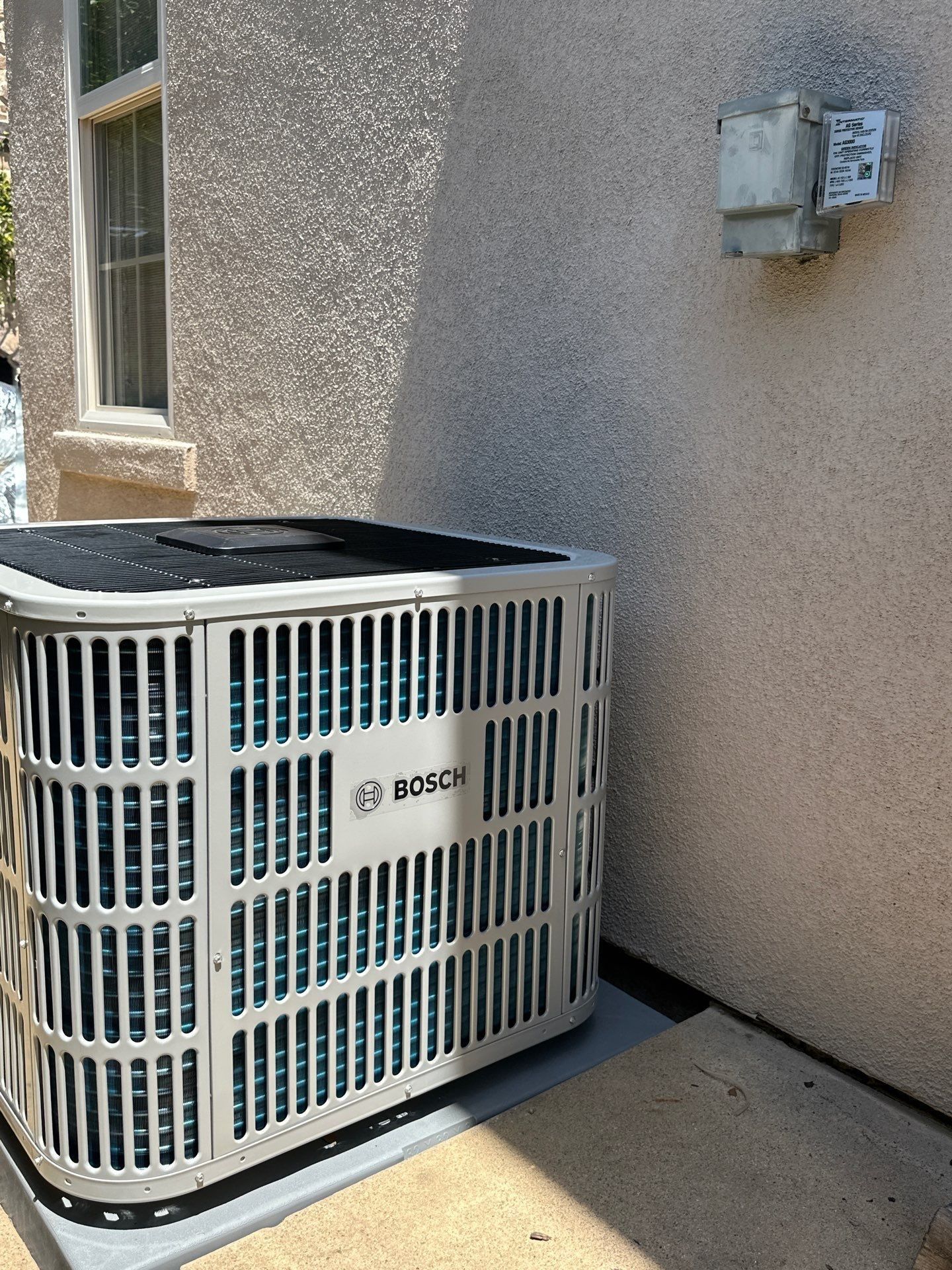 An air conditioning unit by a stucco wall and gas meter.