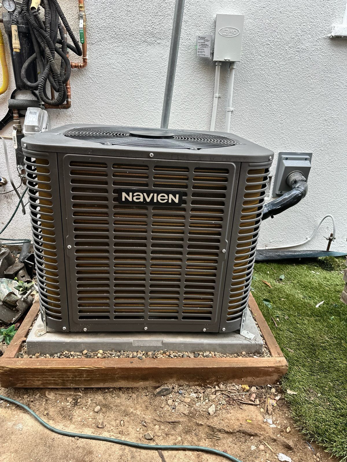 Navien HVAC unit on a concrete pad, against a stucco wall and greenery.