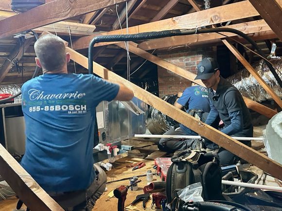 Man points at equipment while others watch in a workshop. Gray, black, and orange colors are visible.
