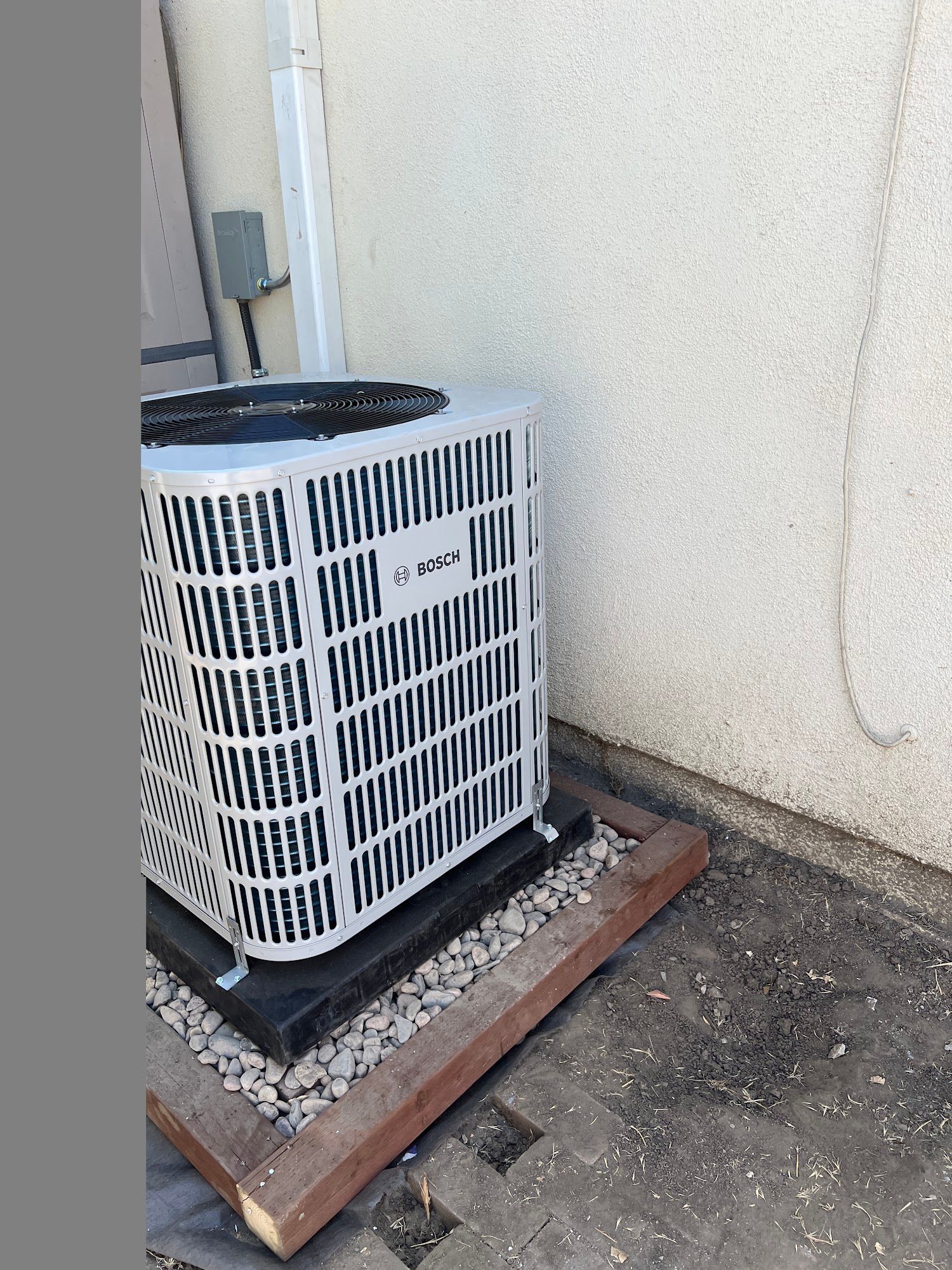 AC unit next to a light-colored stucco wall on a wooden base with gravel.