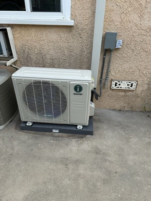 Air conditioning unit on a concrete pad next to a wall. Power outlets and conduit visible.