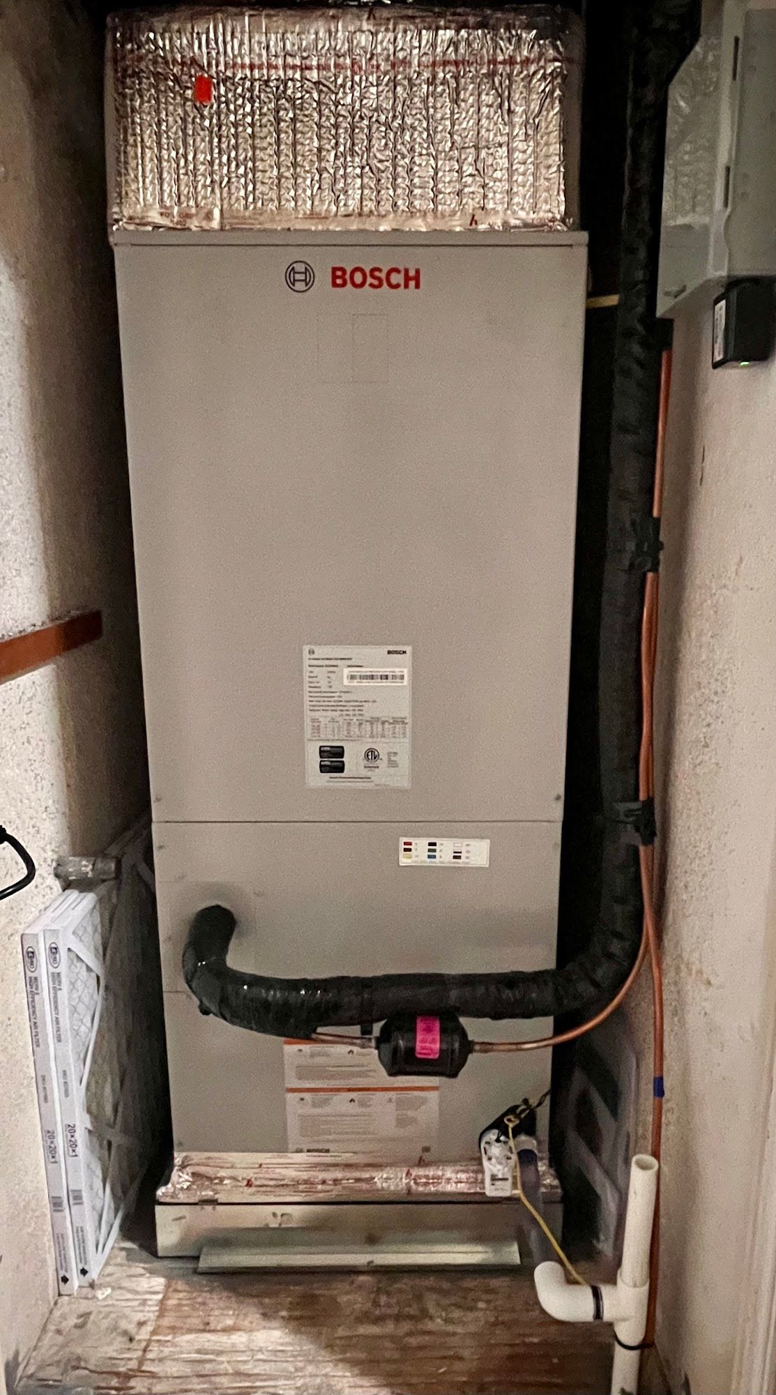 A Bosch furnace unit in a confined space with a ventilation pipe and gas line.