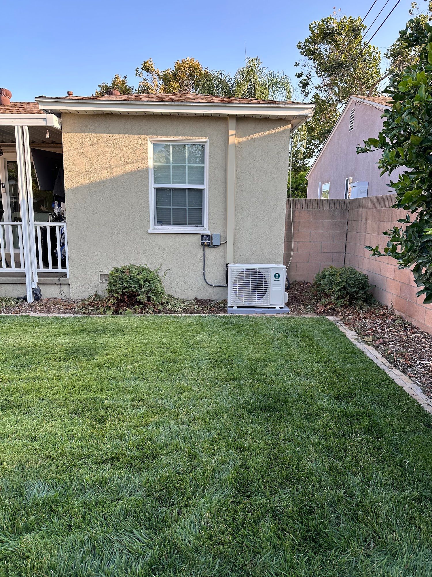 Backyard view of a house with a window, AC unit, and green lawn.