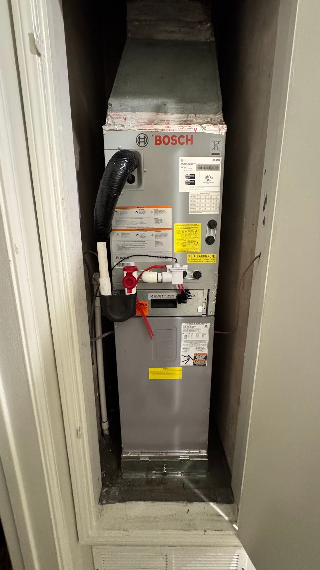 A BOSCH HVAC unit installed inside a closet. Silver metal with black ductwork and red shut-off valves.