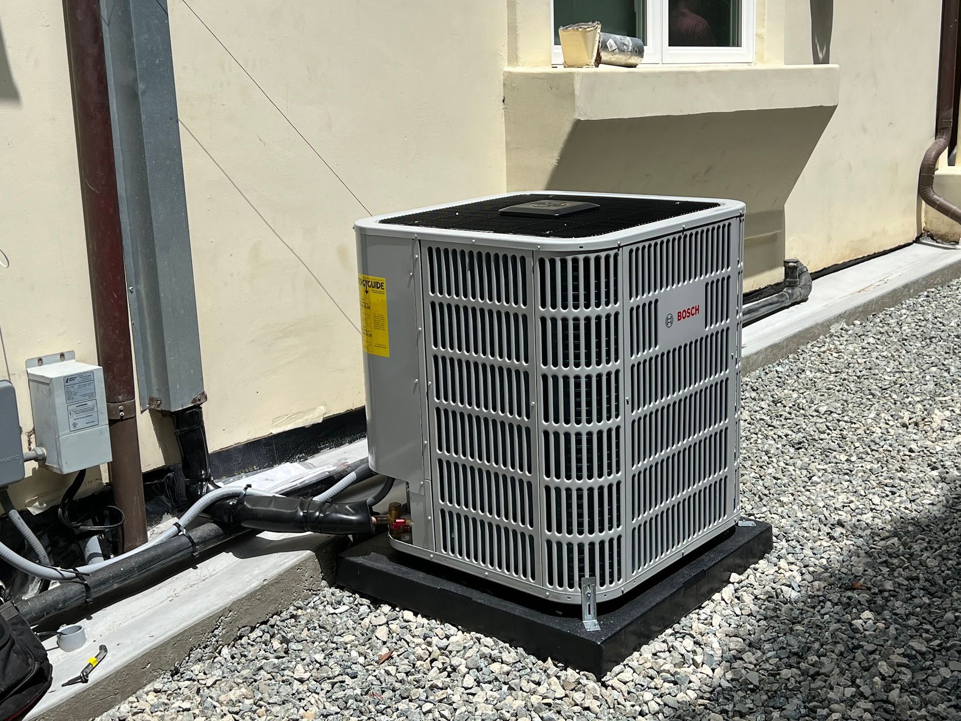 Air conditioning unit on a black base, next to a building with gravel and pipes.