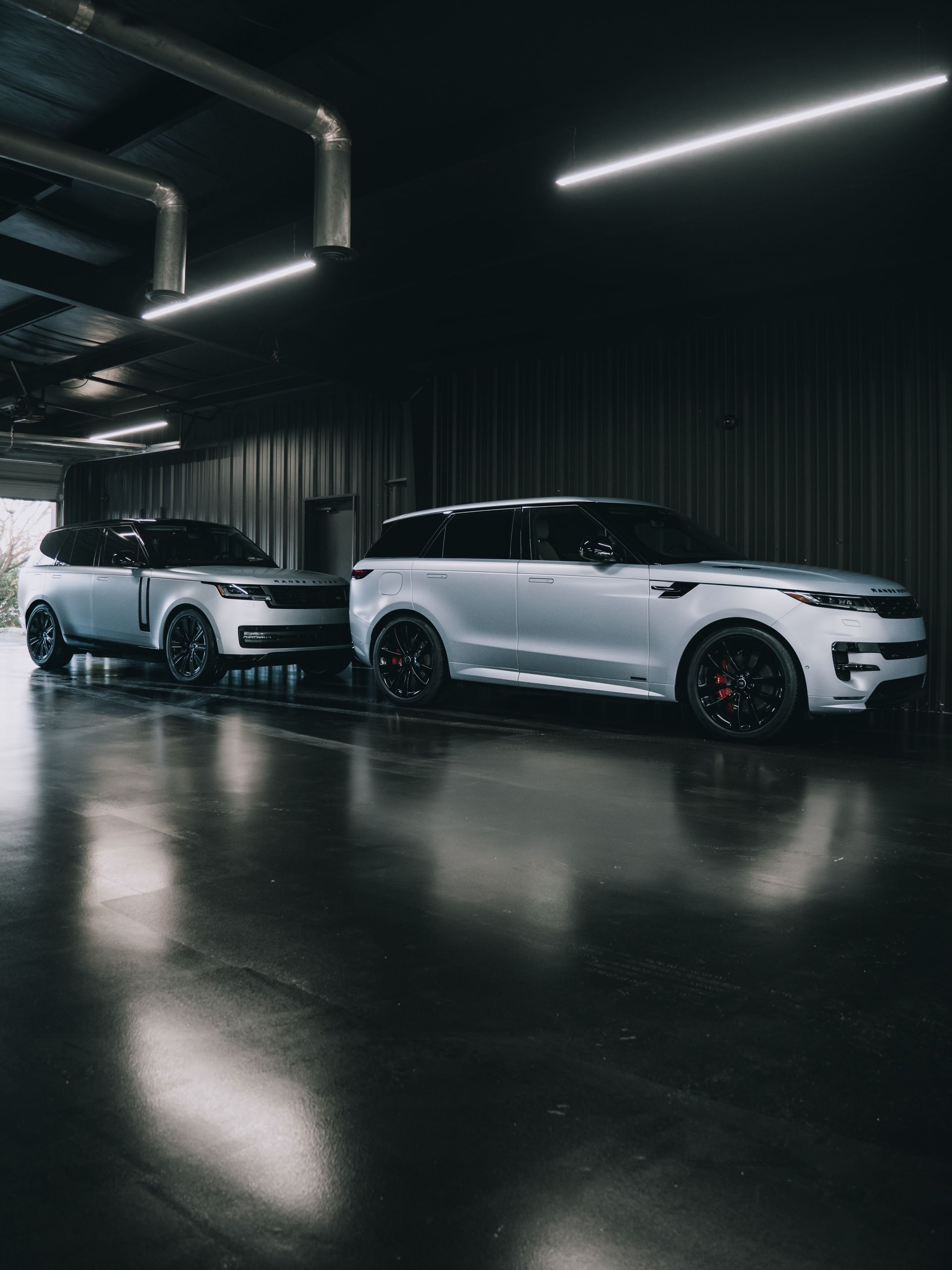 Two silver Range Rover SUVs parked inside a dark, modern garage with reflective flooring.