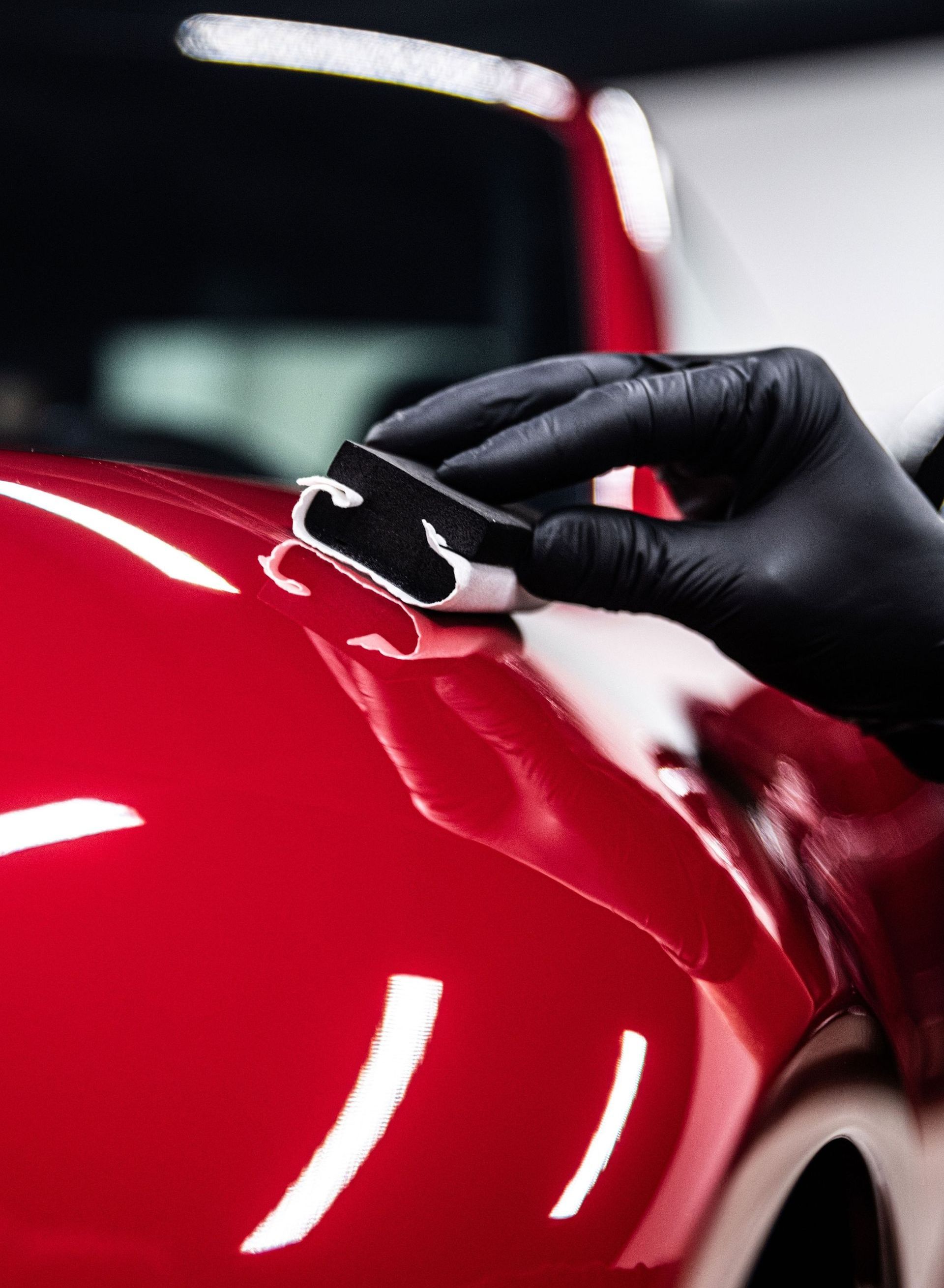 A person wearing black gloves is polishing a red car.