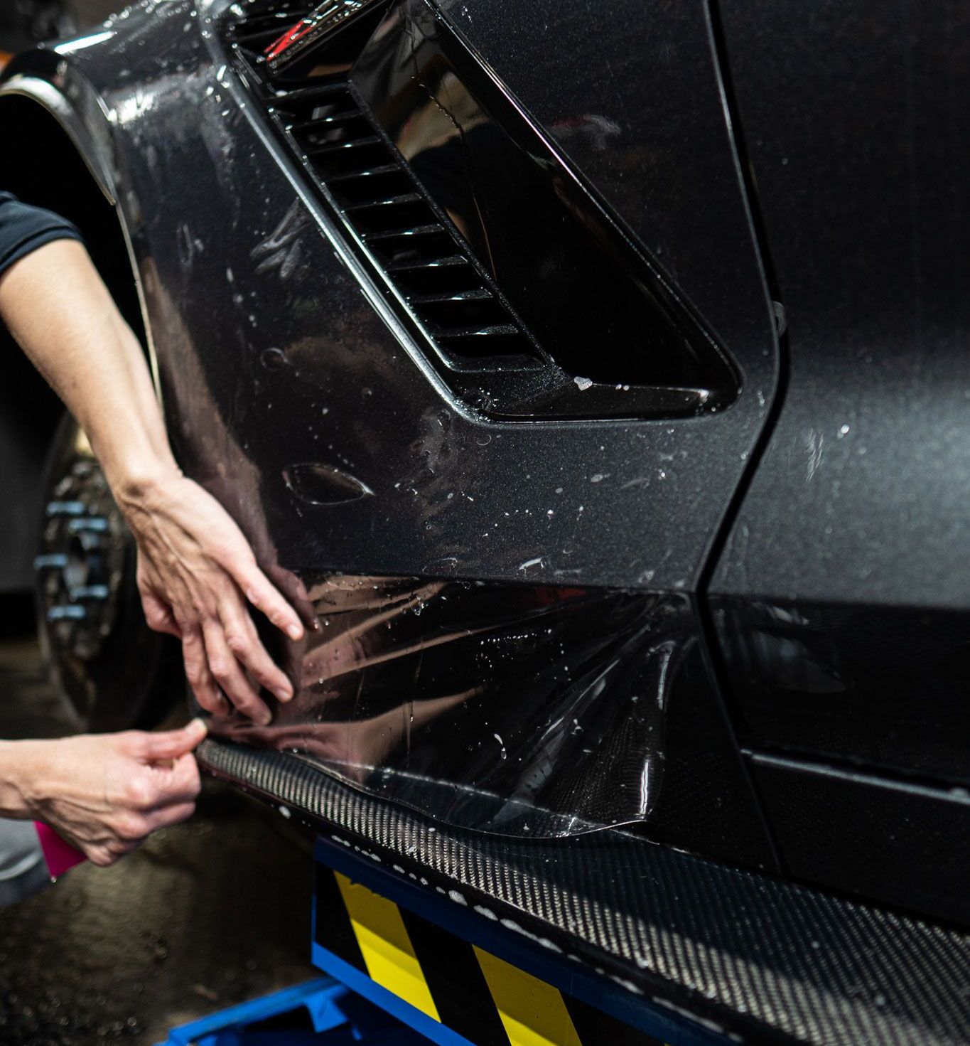 A person is applying a protective film to a black car