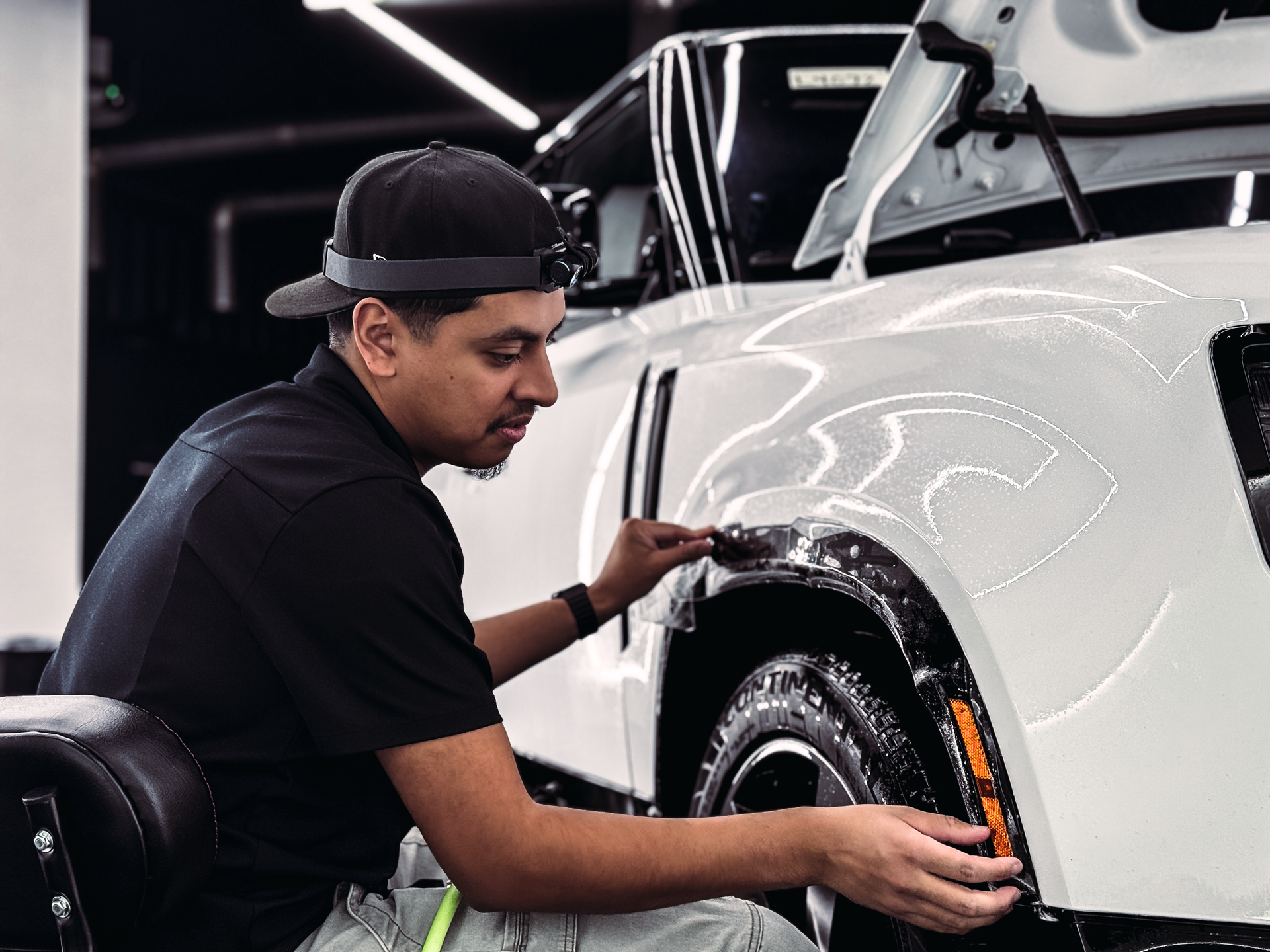 Man installing protective film on a white car bumper in a garage.