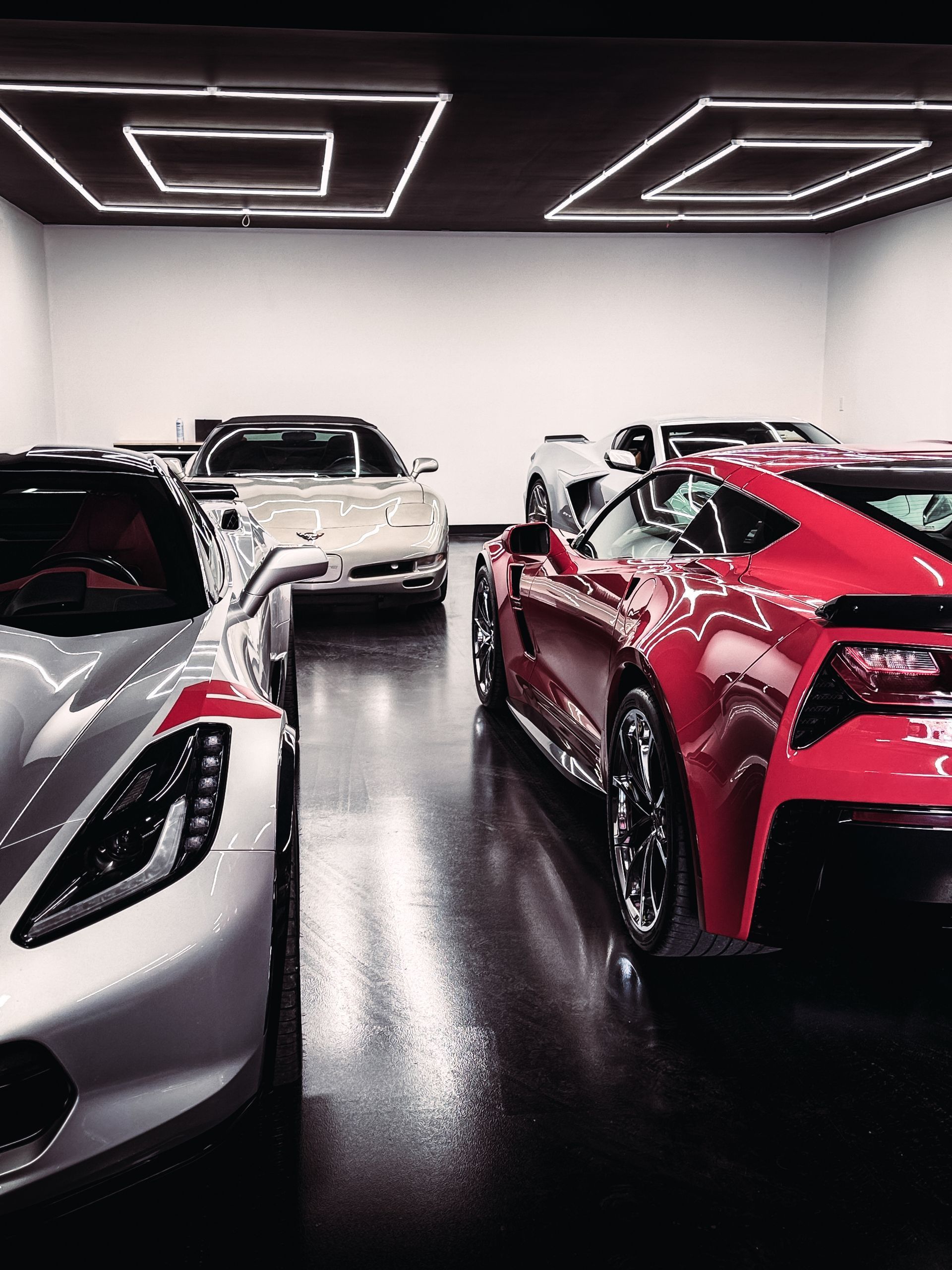 A white car is parked in a garage next to a black car.