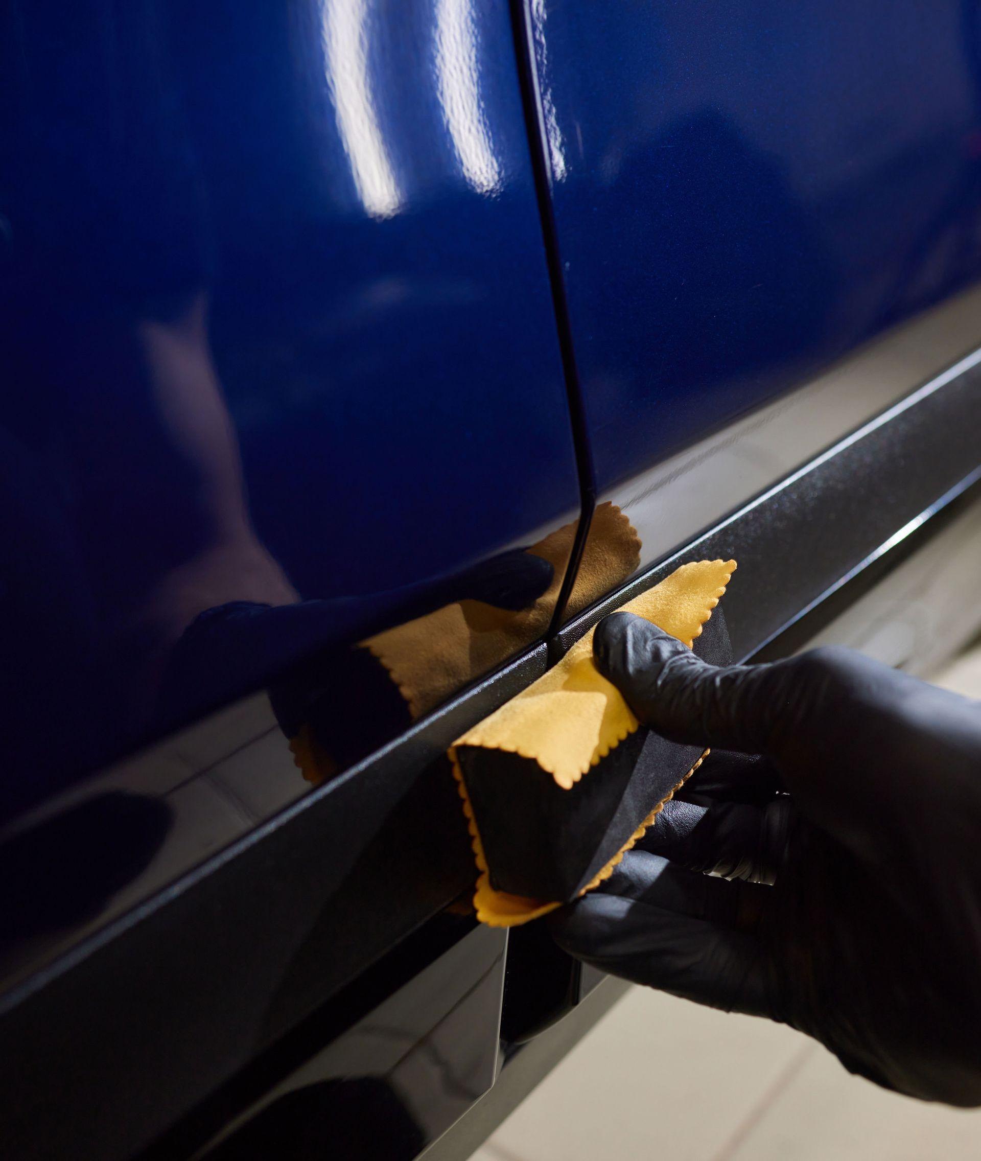 A person wearing black gloves is polishing the hood of a red car.