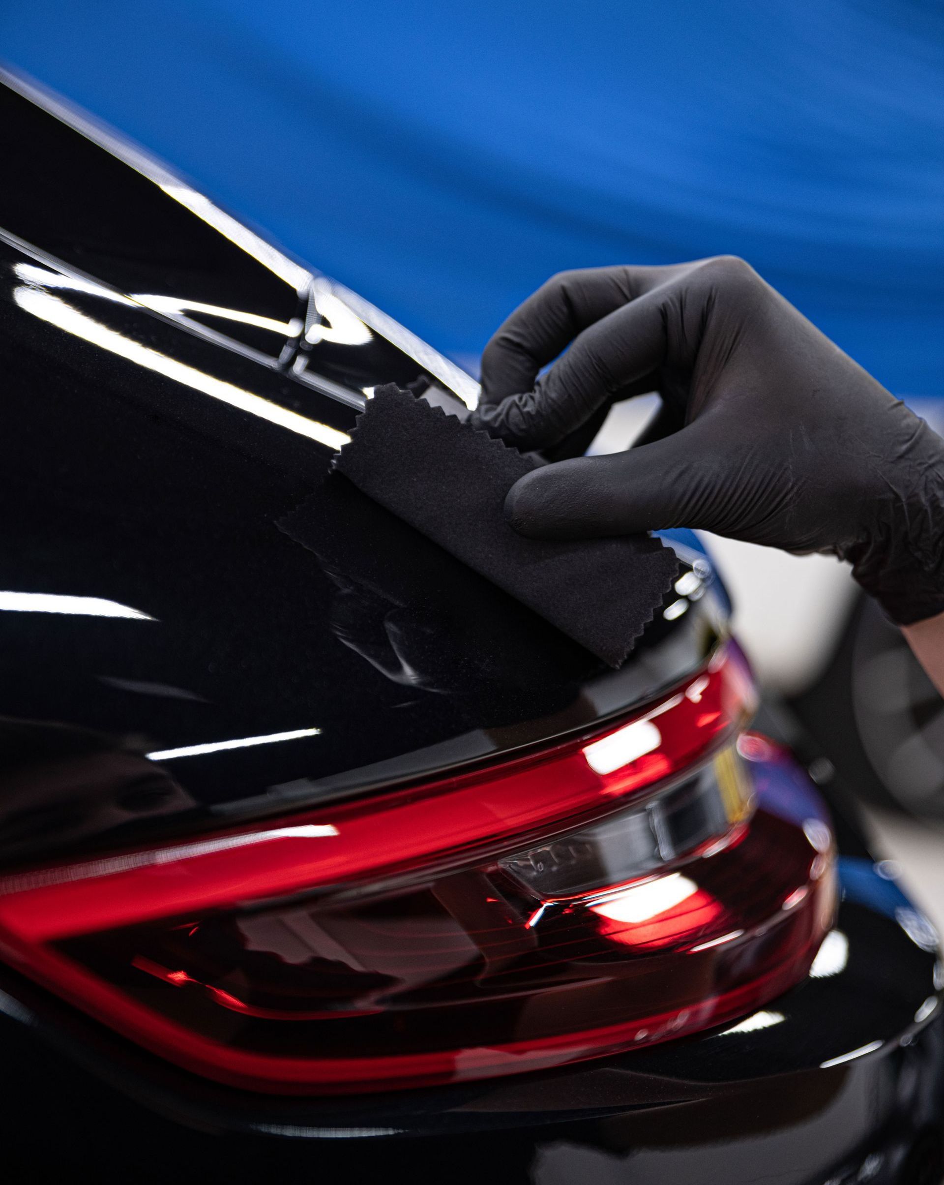 A person is polishing the hood of a blue car.