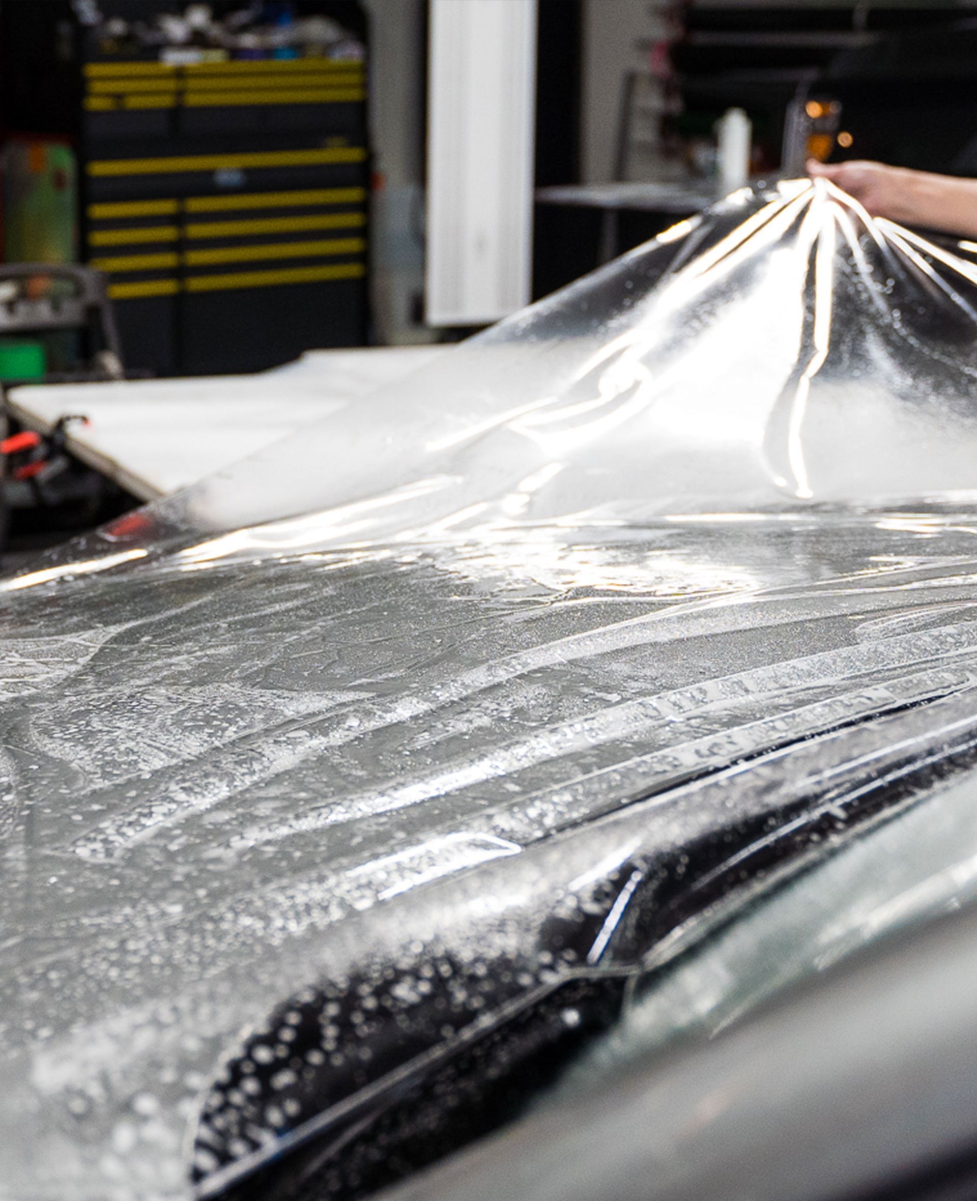 A person is covering the hood of a car with plastic wrap.