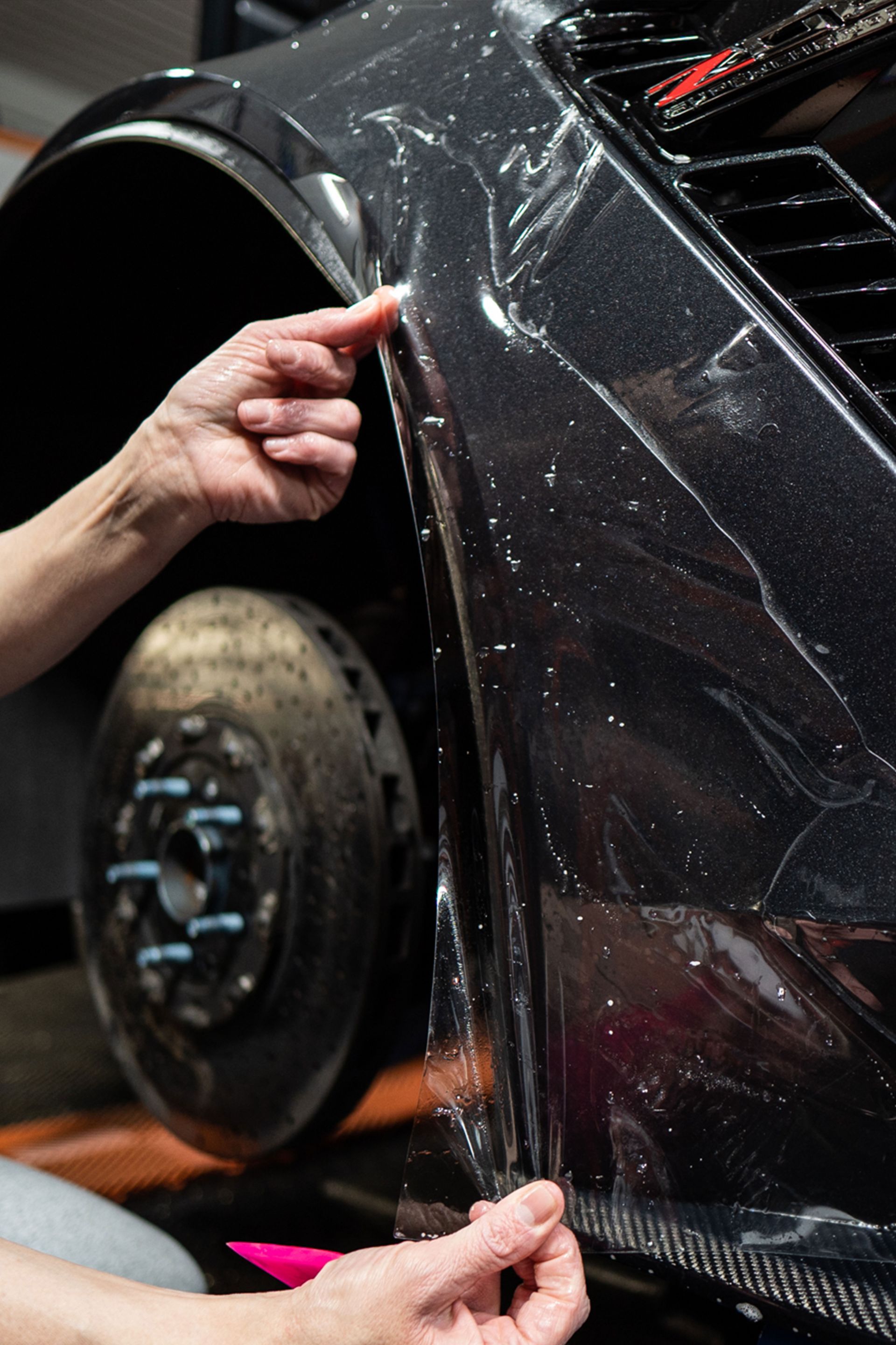 A person is applying a clear plastic covering to a car 's fender.