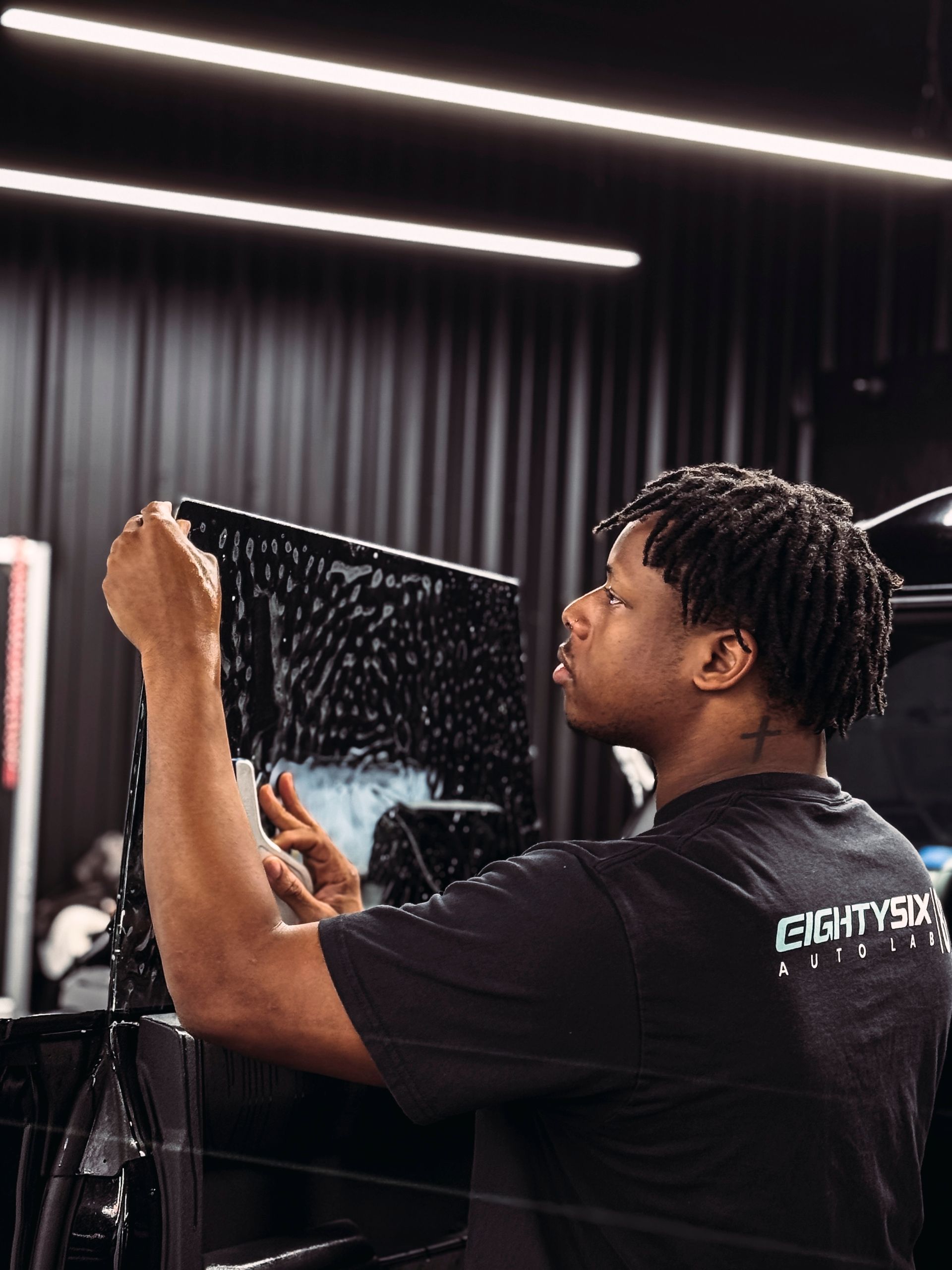 A person in a black shirt is applying window tint in a shop.
