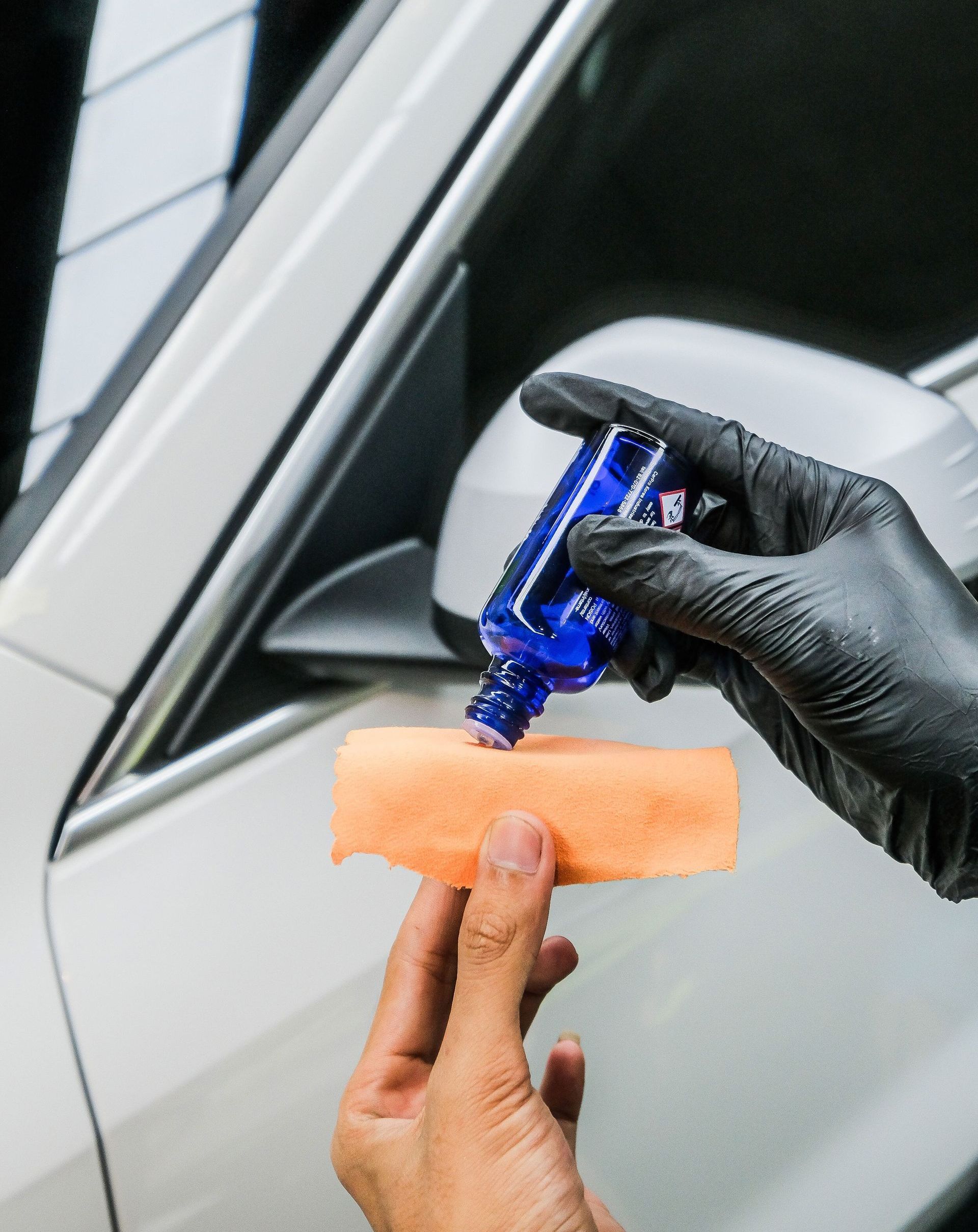 A person wearing black gloves is holding a bottle of blue liquid