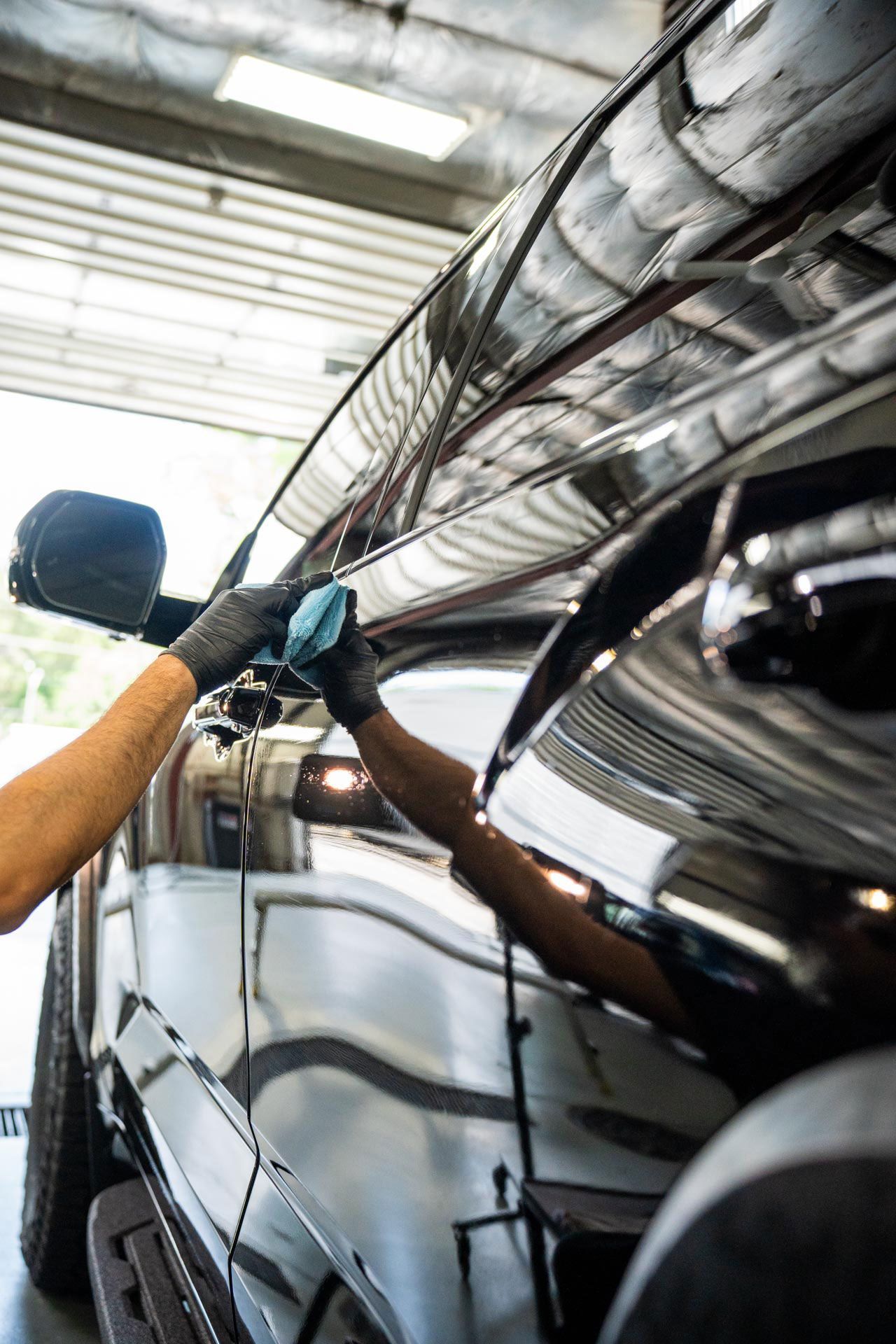 A man is polishing the side of a car in a garage.