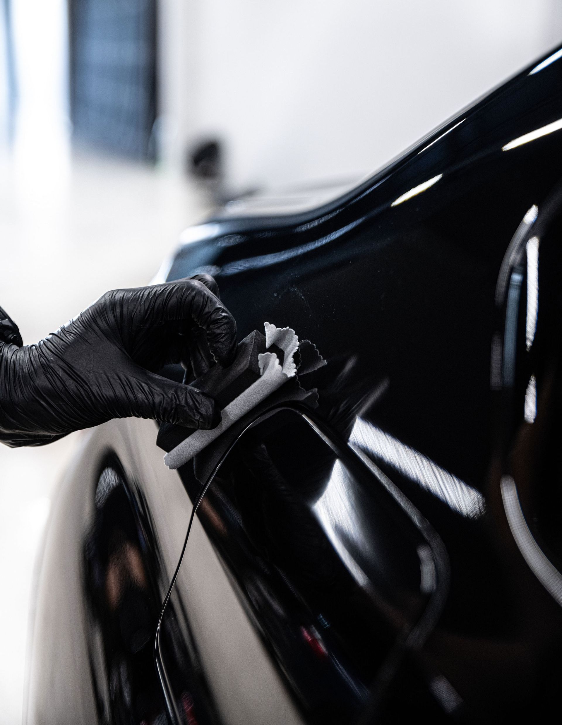 A person is polishing a black car with a sponge.