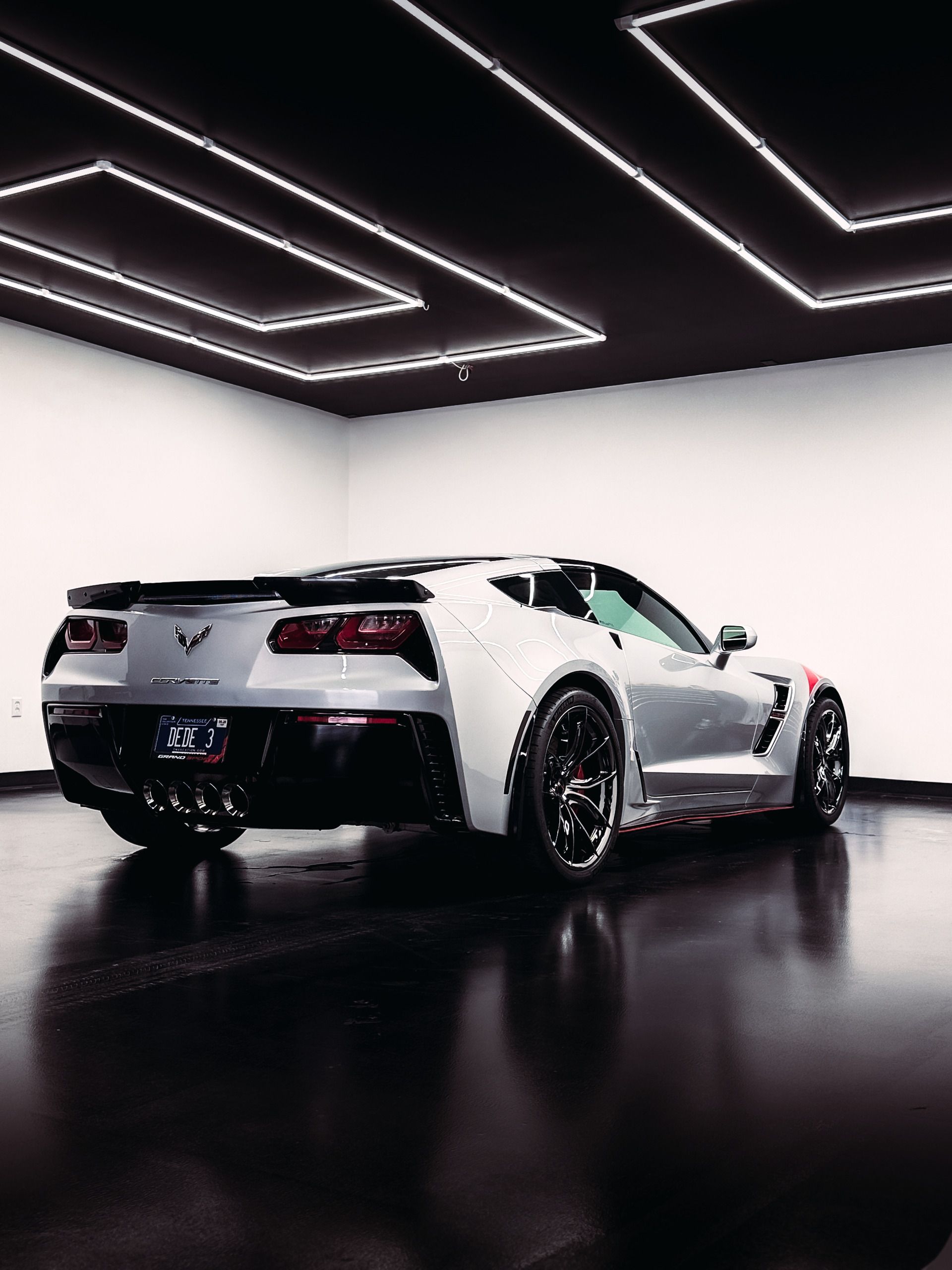 Silver sports car in a modern white and black showroom, with overhead neon lighting.