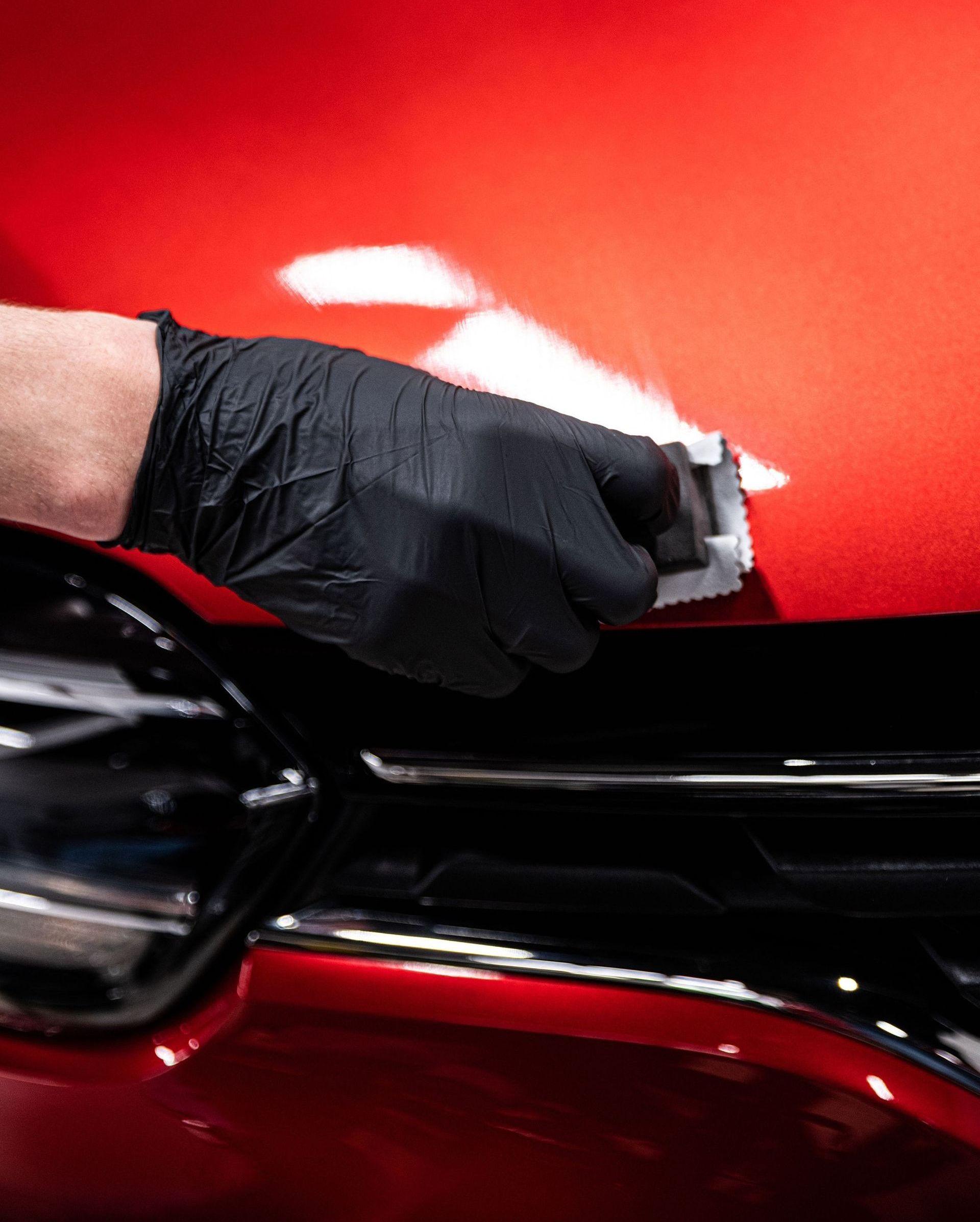 A person wearing black gloves is polishing the hood of a red car.