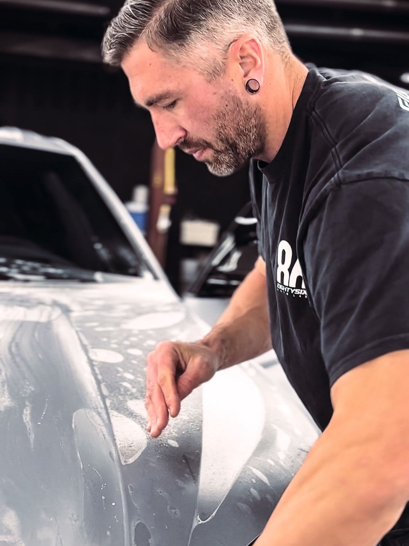 Man applying film to car hood, focused, indoor setting.