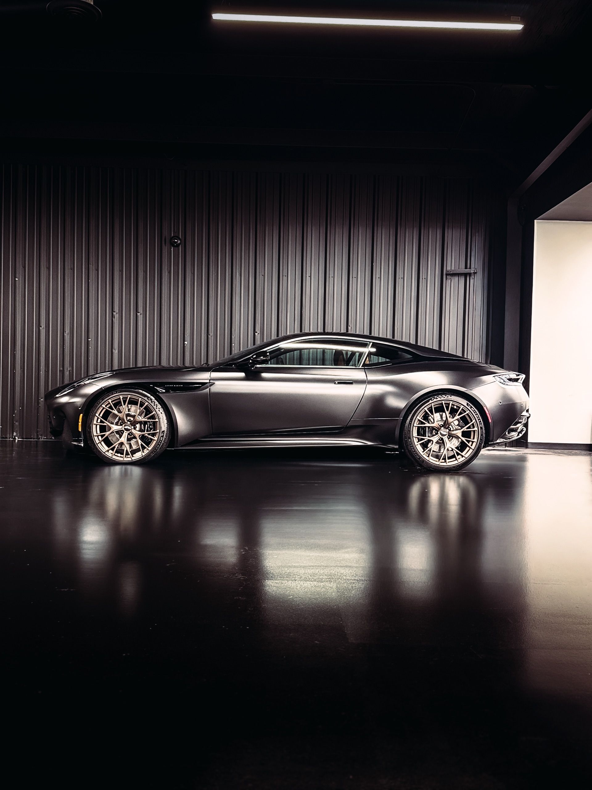Gray luxury sports car parked inside a dark, modern garage with reflective flooring.