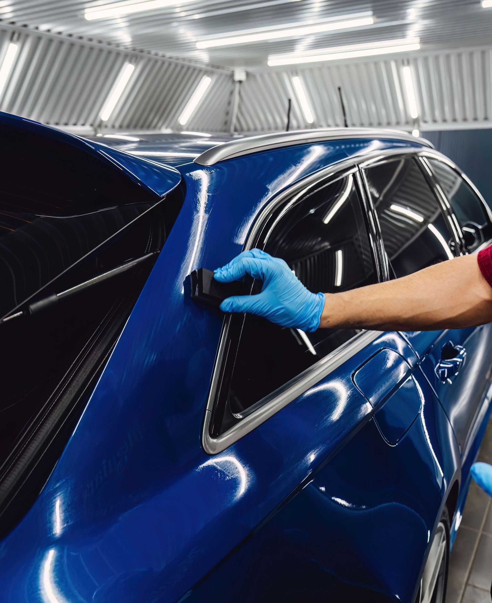 A person is polishing a blue car in a garage.