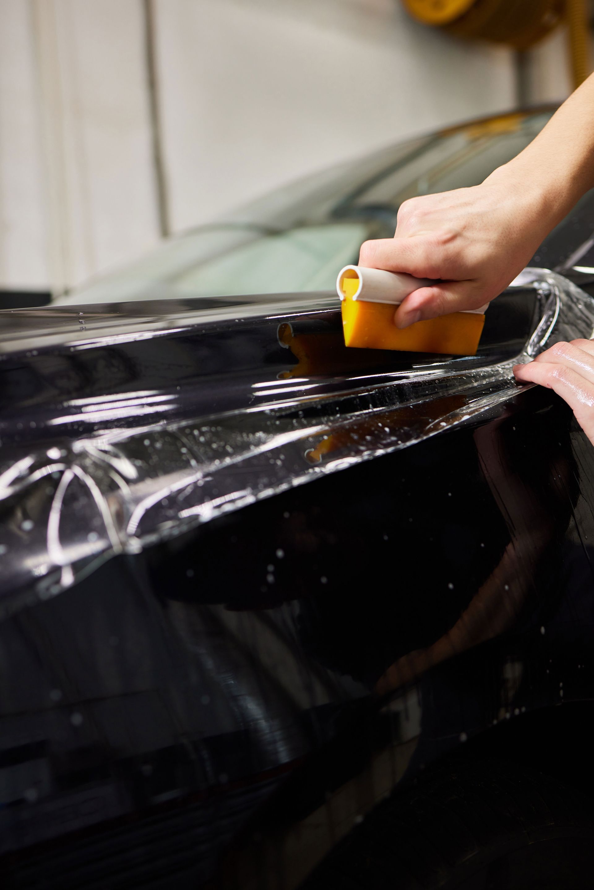A person is applying a protective film to a black car.