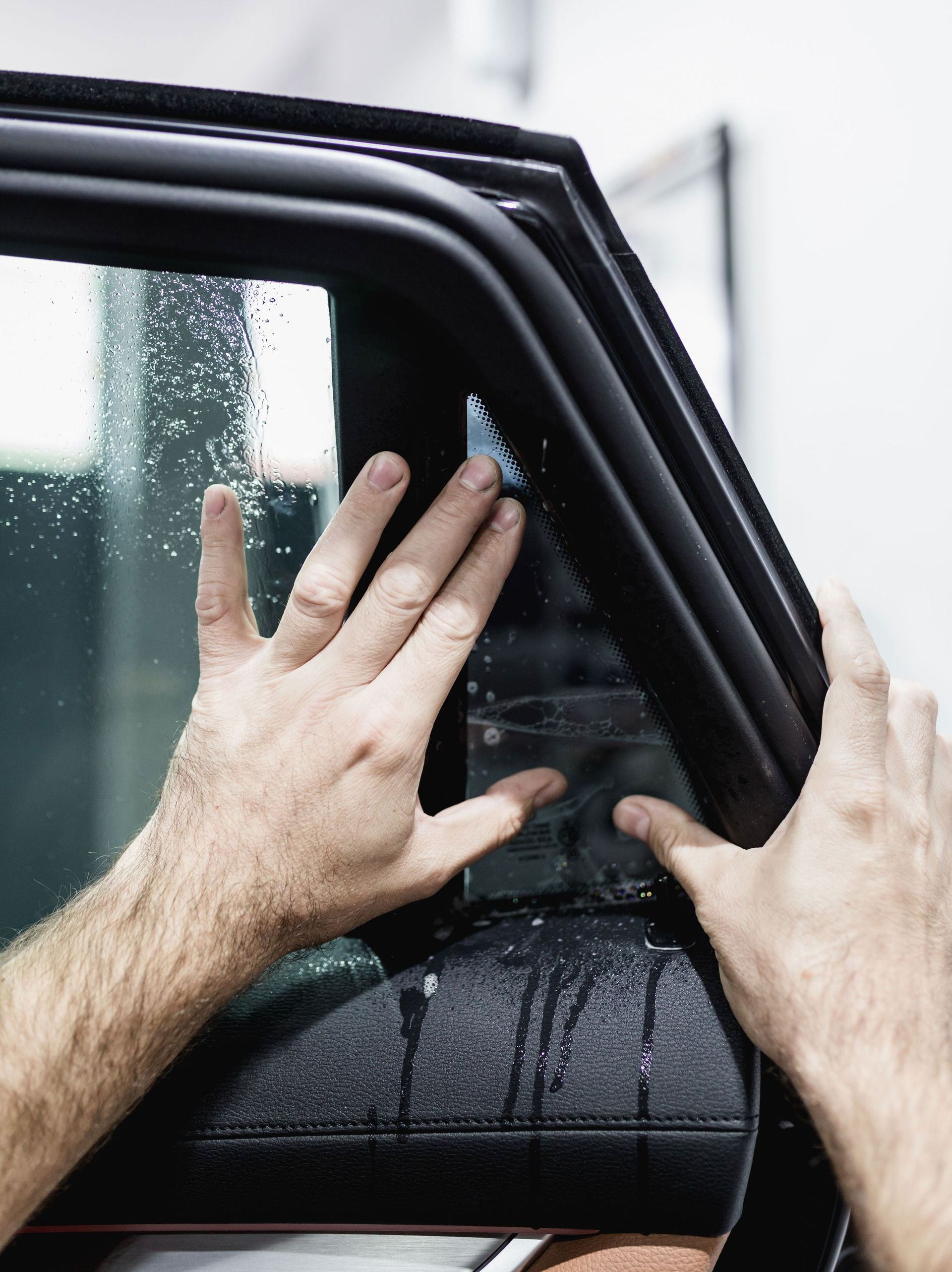 A person is applying tinted window film to a car window.