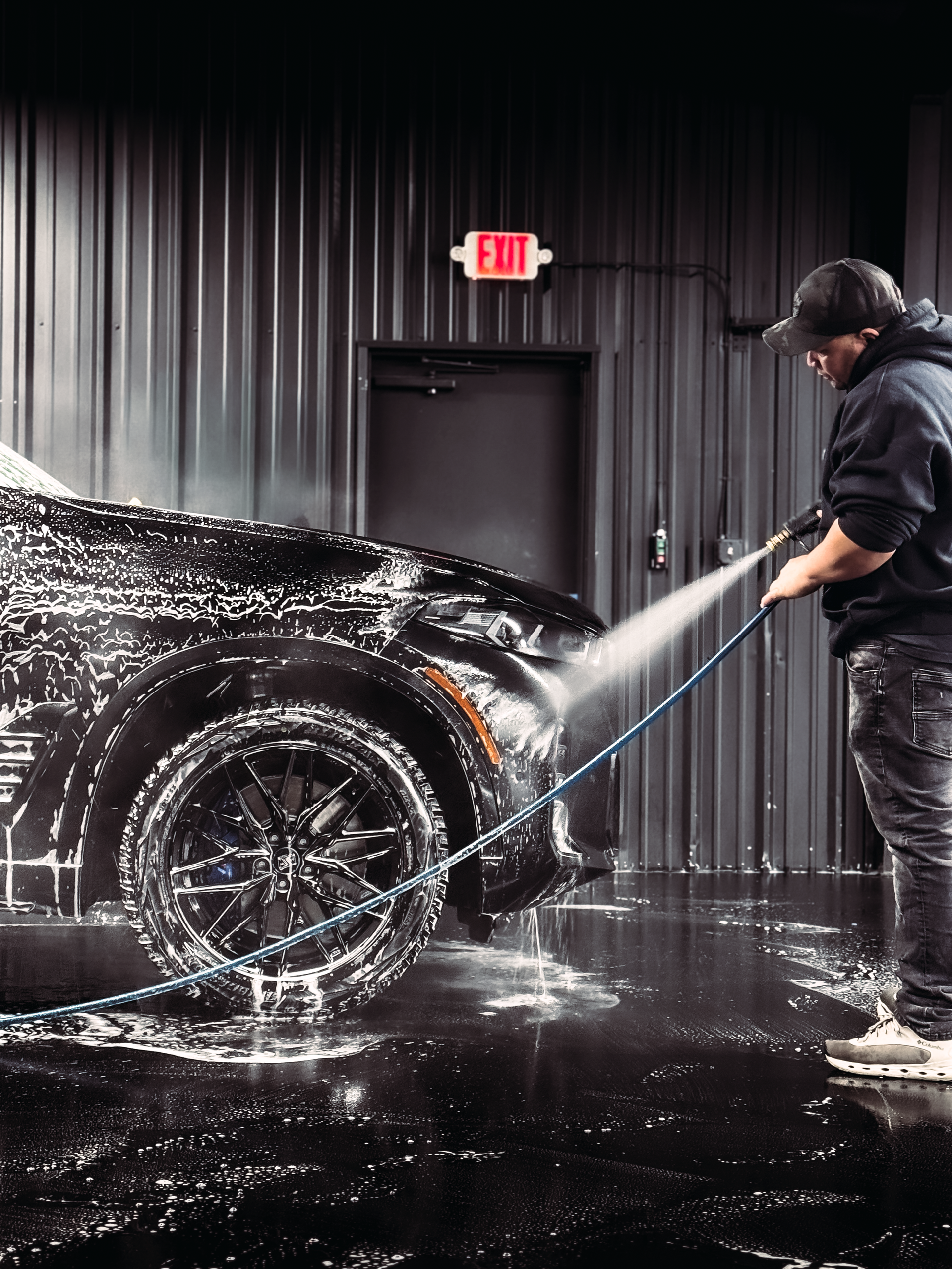 A man is washing a car with a hose in a car wash.