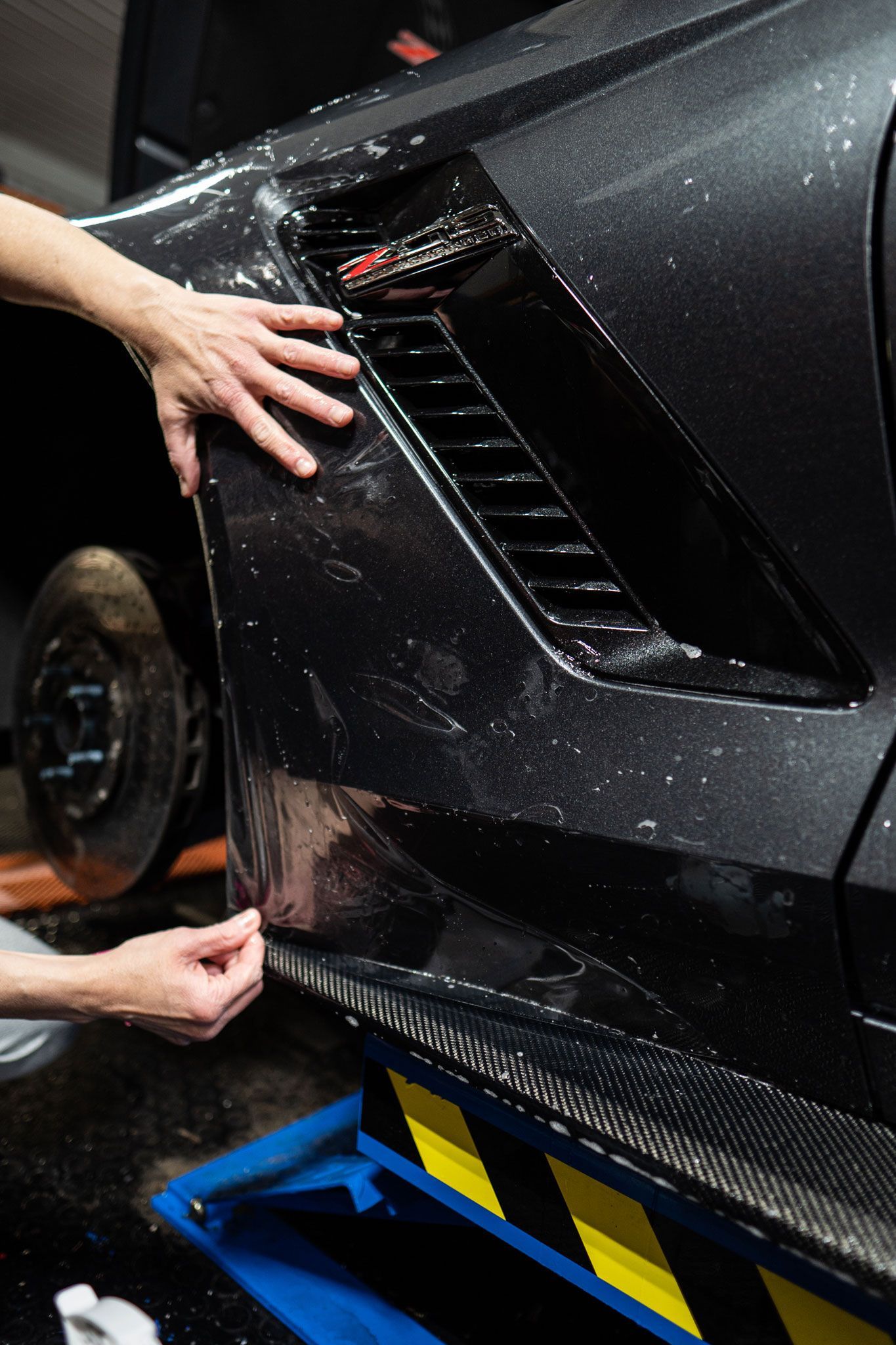 A person is applying a protective film to the side of a car.