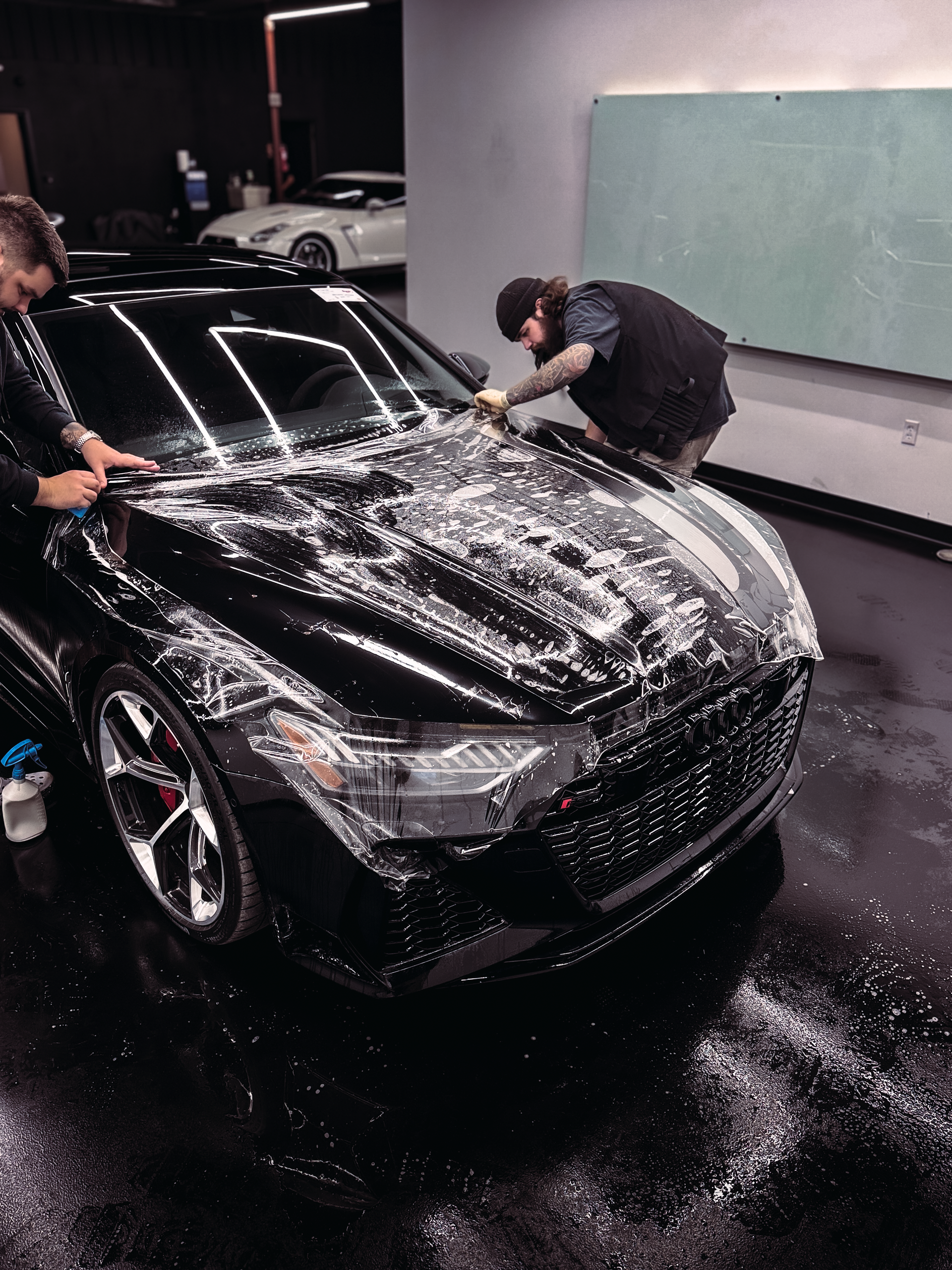 A man is applying a protective film to the hood of a car.
