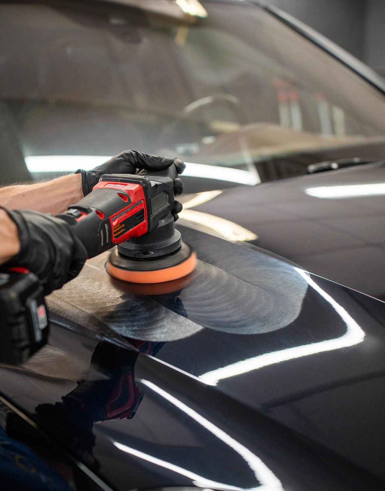A person is polishing the hood of a car with a machine.