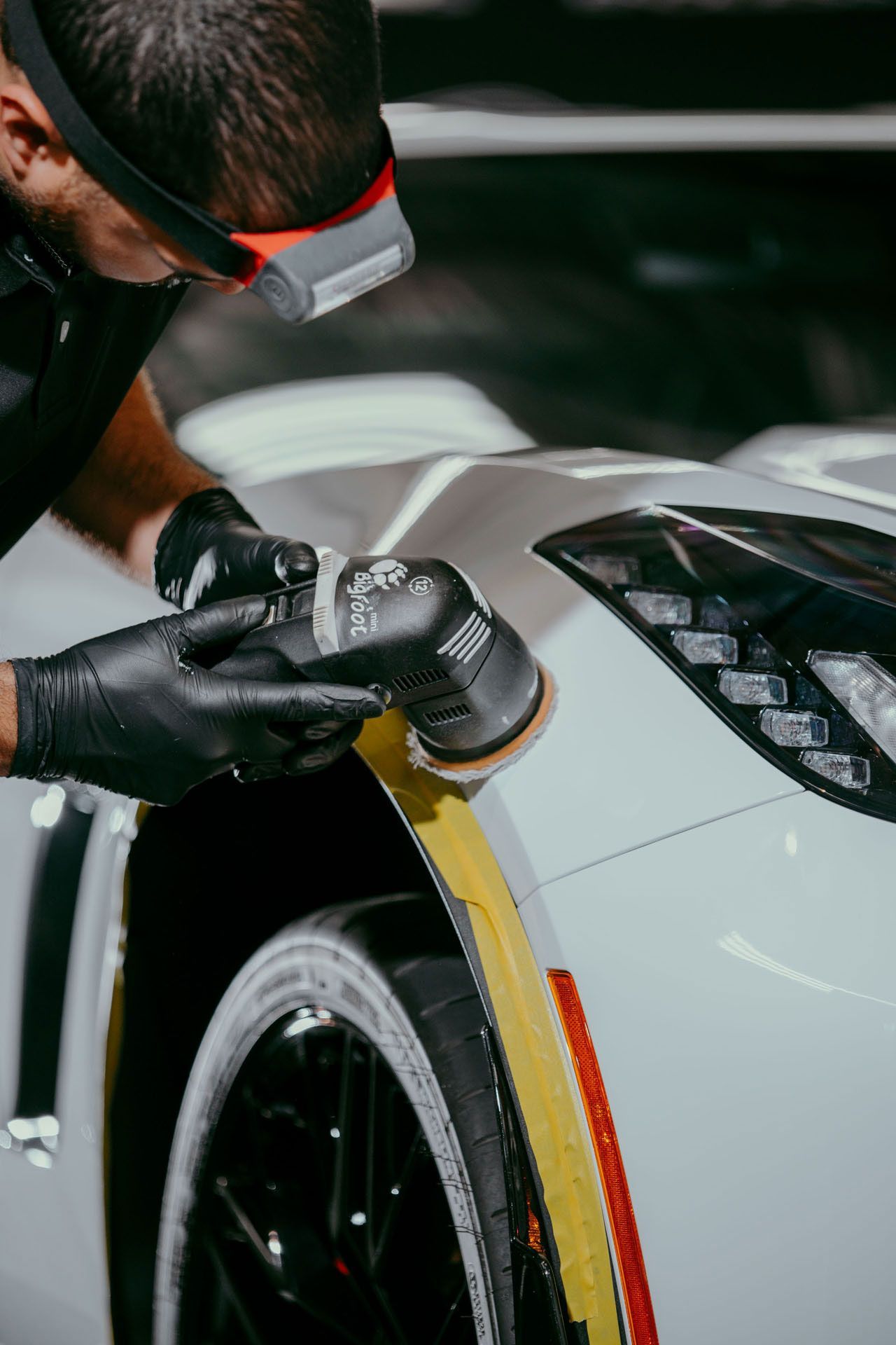 A man is polishing a white car with a polisher.