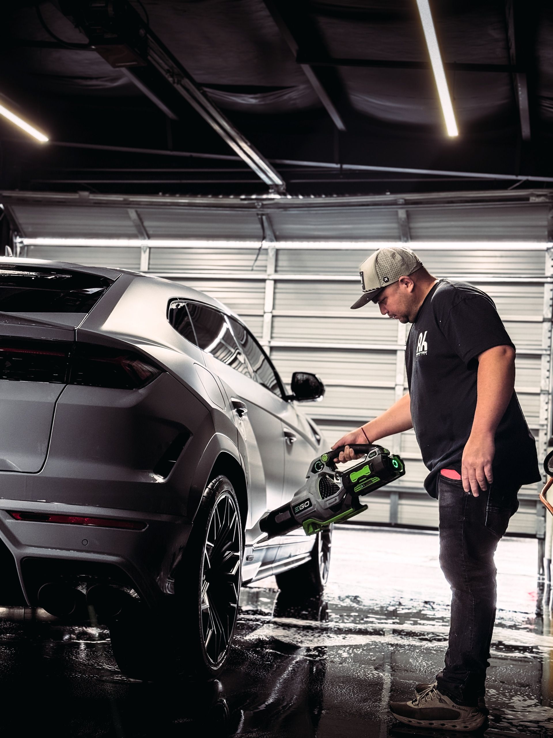 Man washing a silver car with a green power washer in a garage.