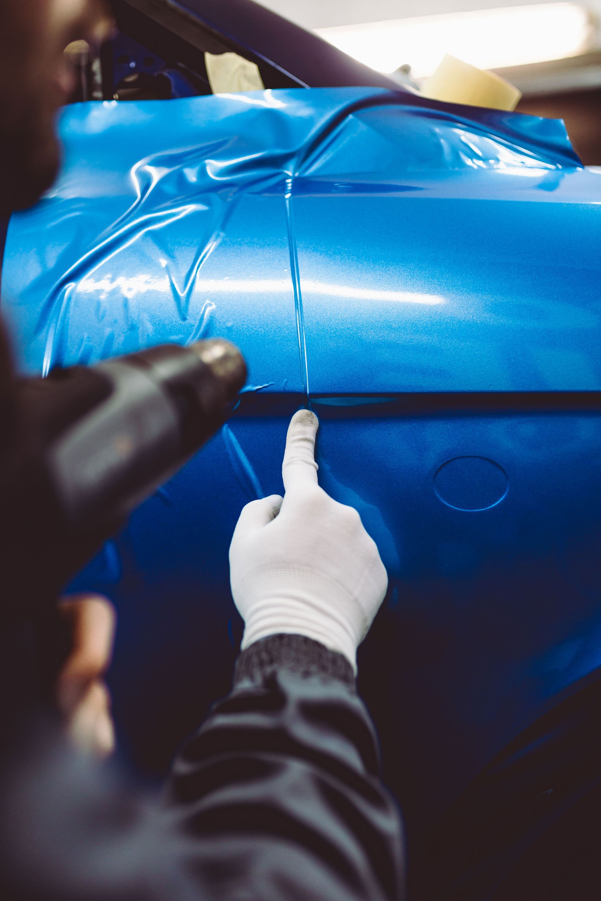 A person is wrapping a blue car with blue tape.
