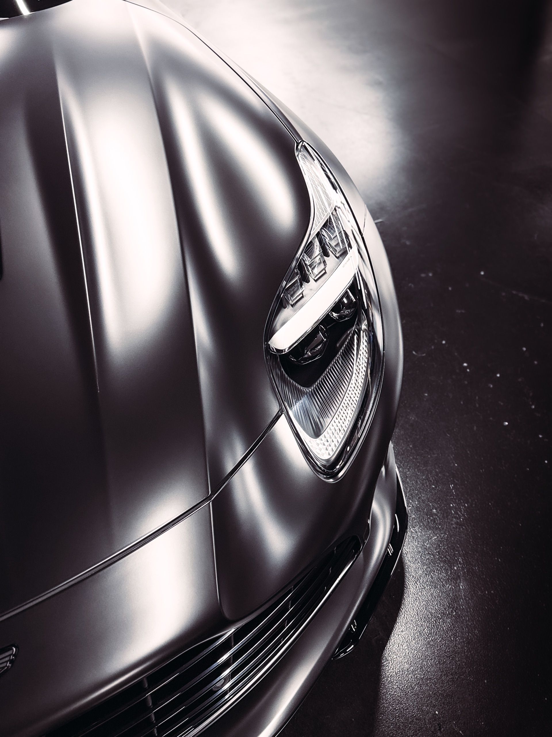Close-up of a silver sports car headlight and hood, reflecting light.