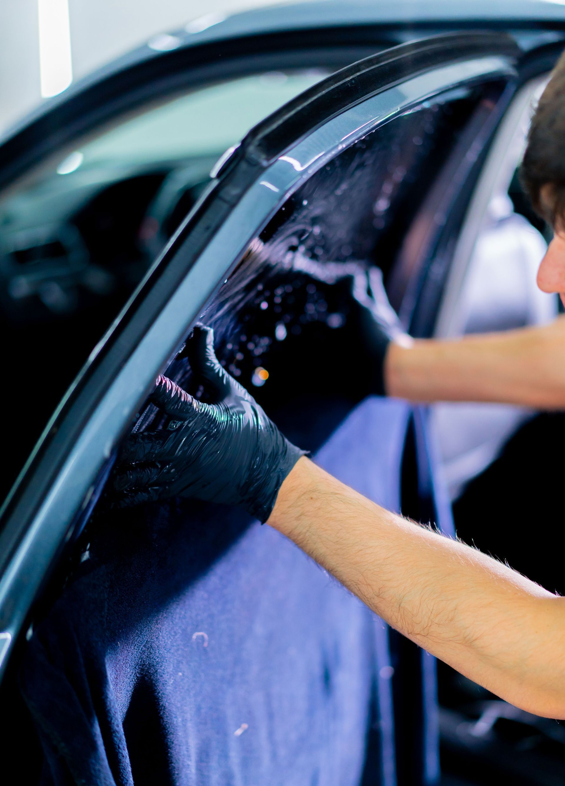 A person wearing black gloves is cleaning a car window.