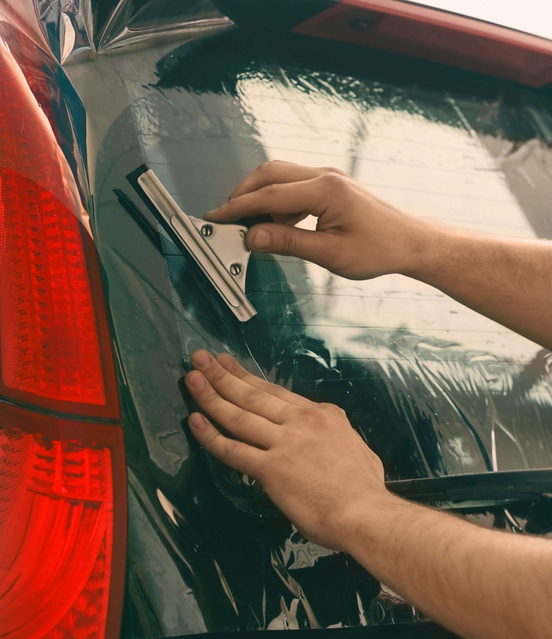 A person is applying window tinting to the back window of a car.