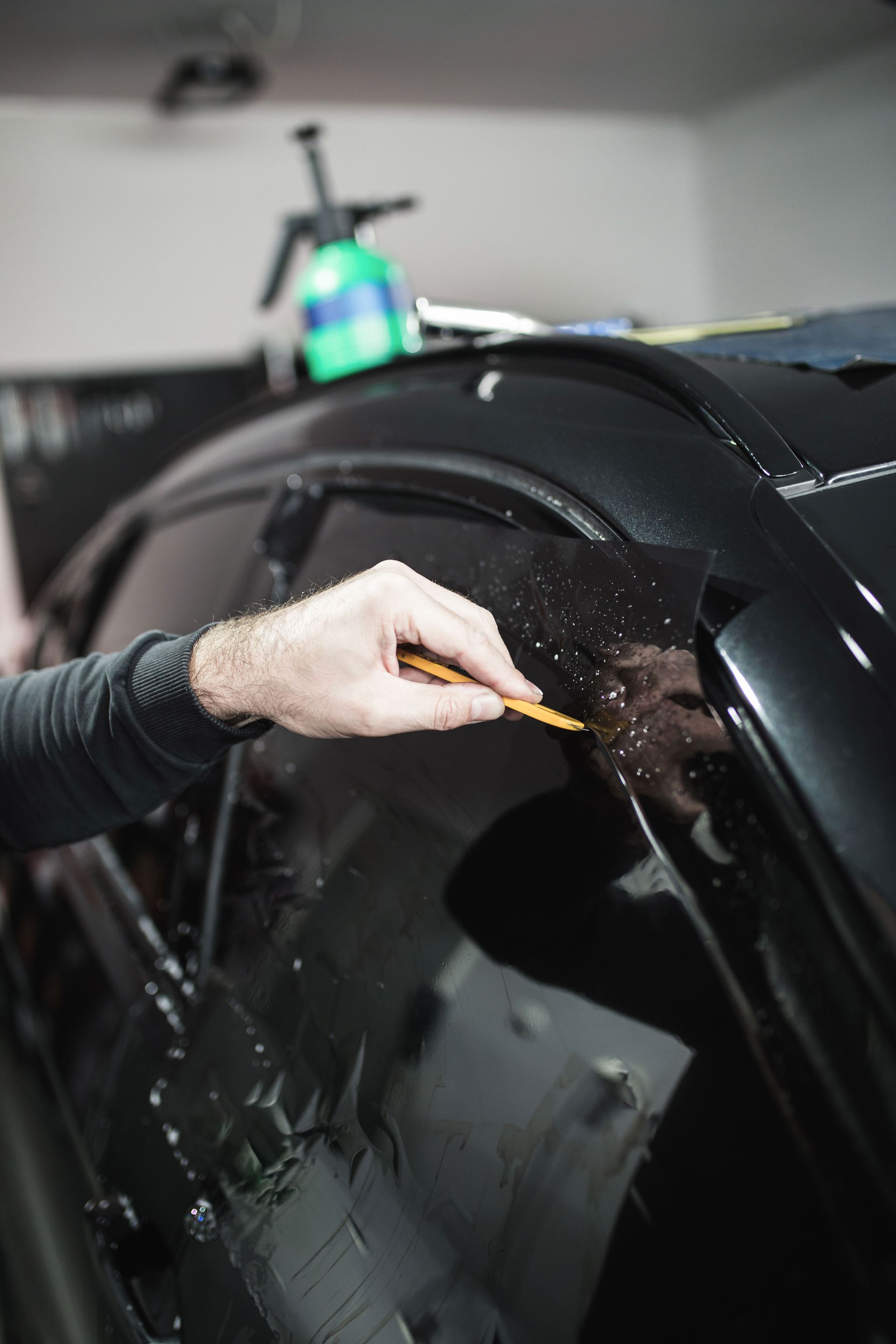 A man is applying tinted window film to a car window.