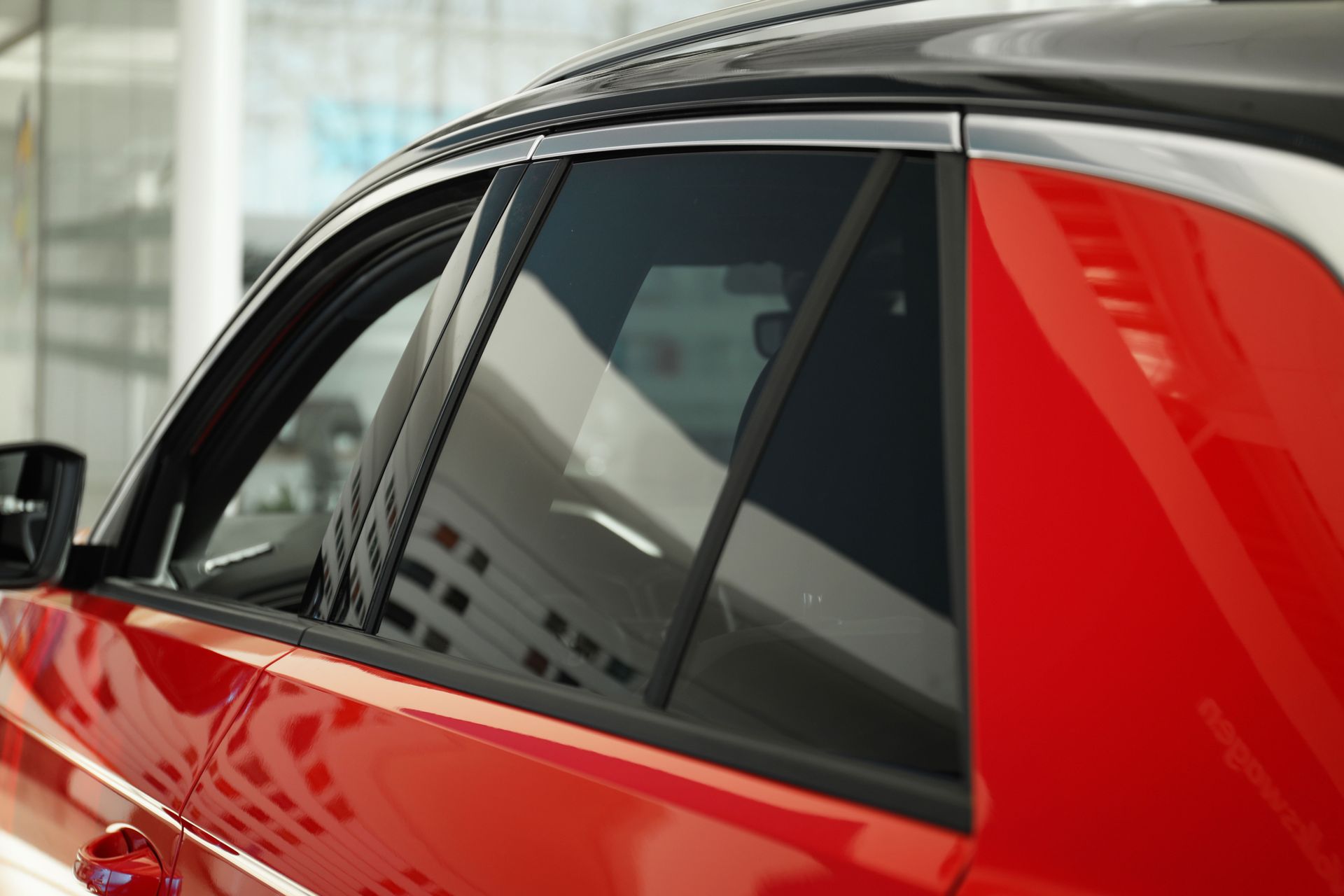 A red car with a black roof is parked in a showroom.