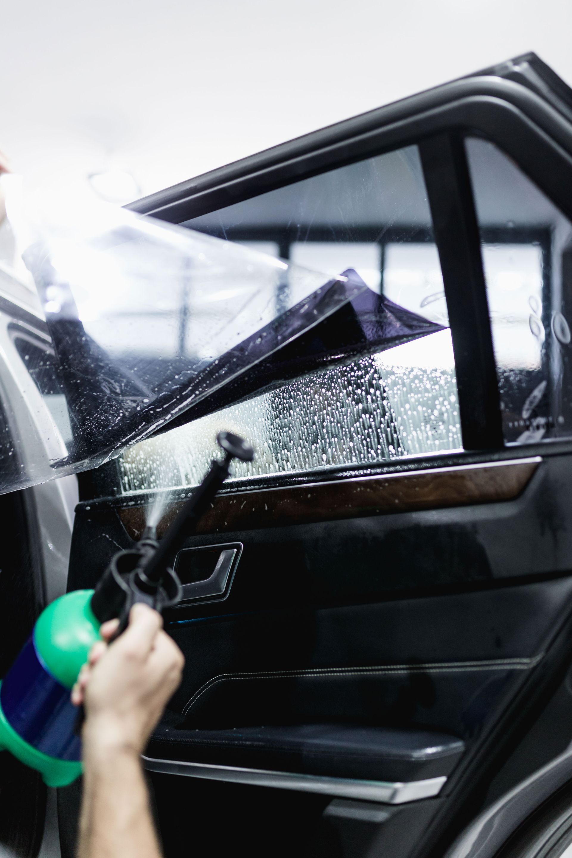 Person spraying soapy water on a car window while applying window tint.